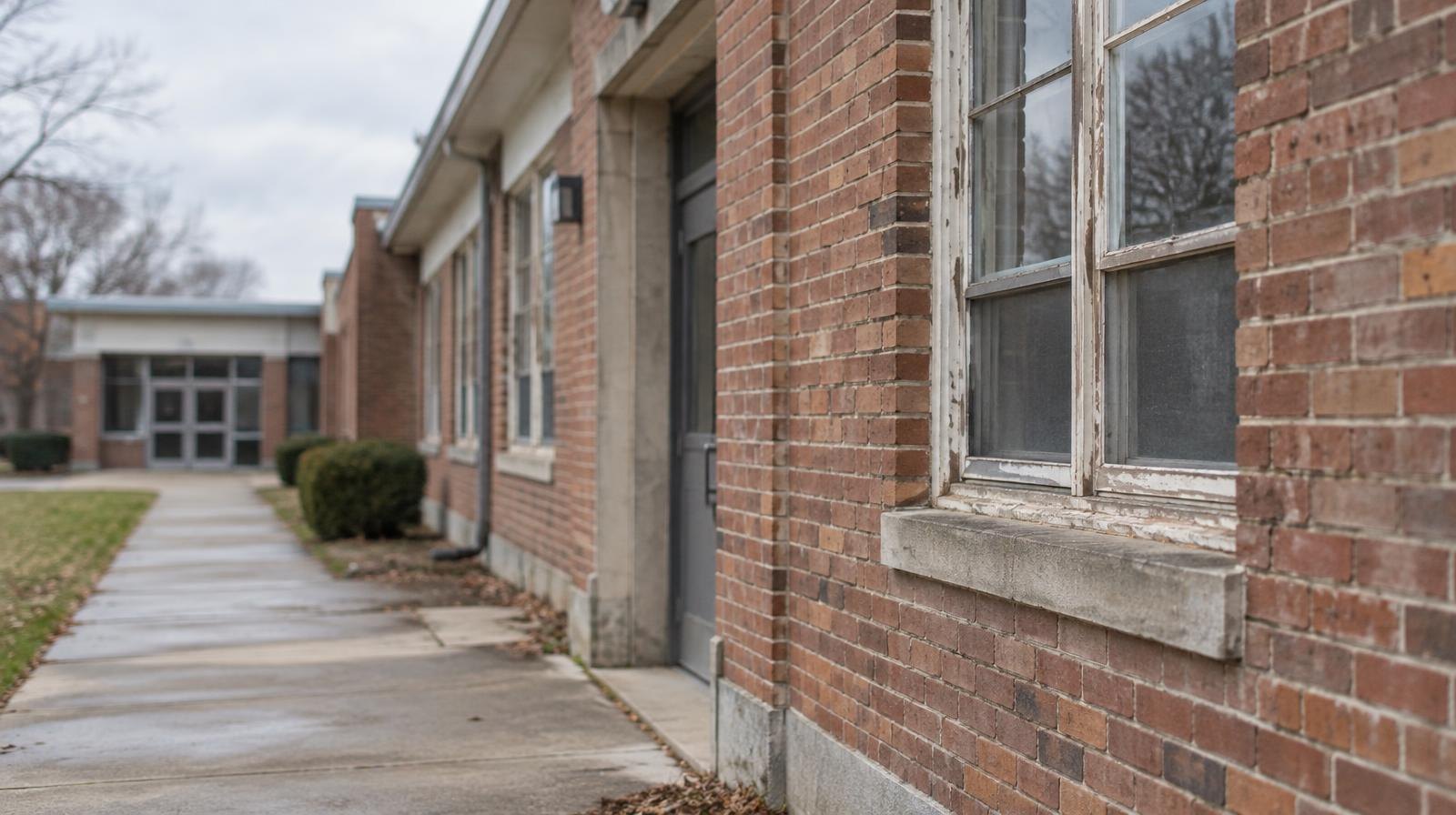 Row of aging school building exteriors with weathered brick walls and worn walkway.
