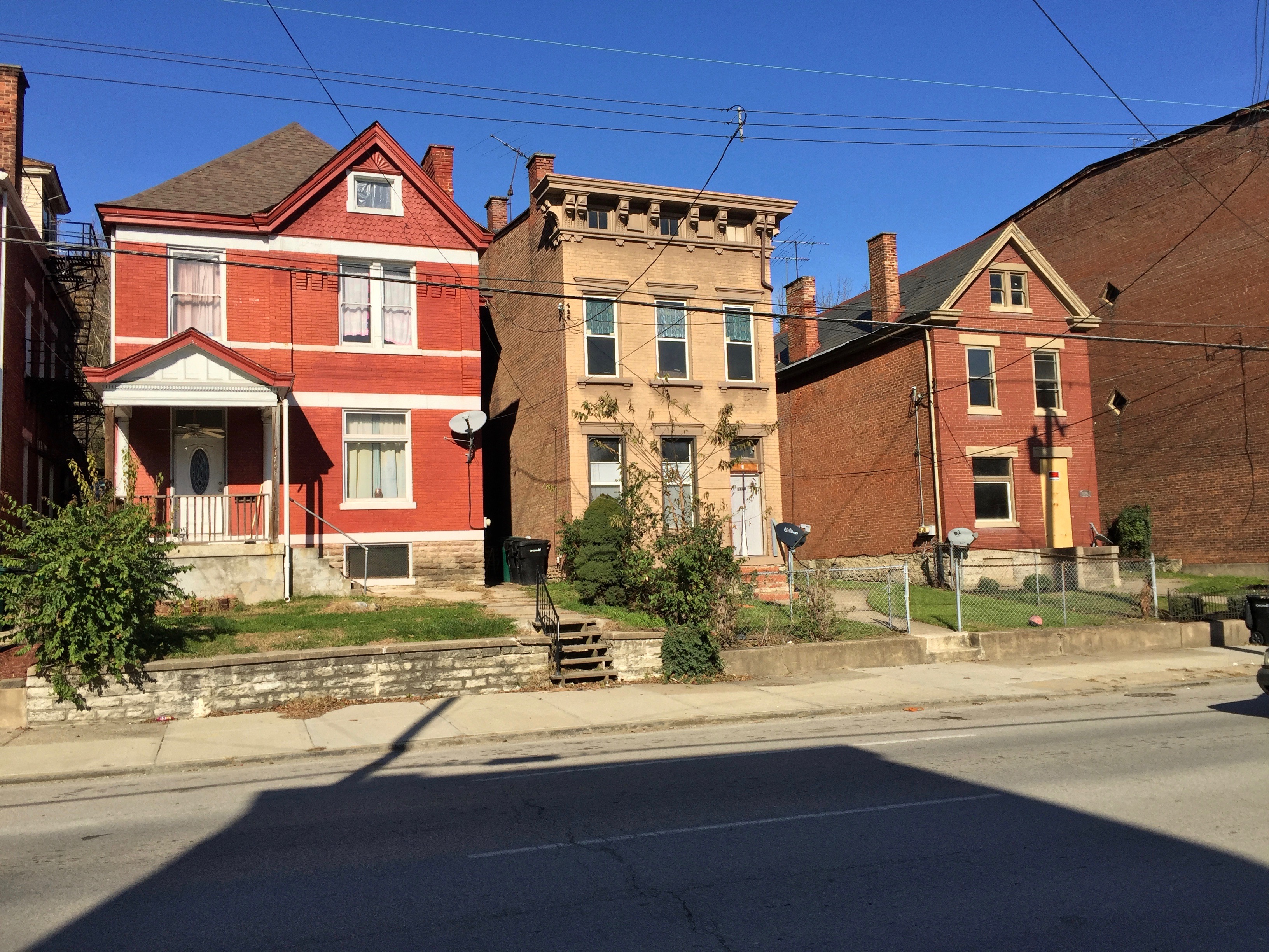 Row of older brick residential buildings of varying styles and sizes along a city street.