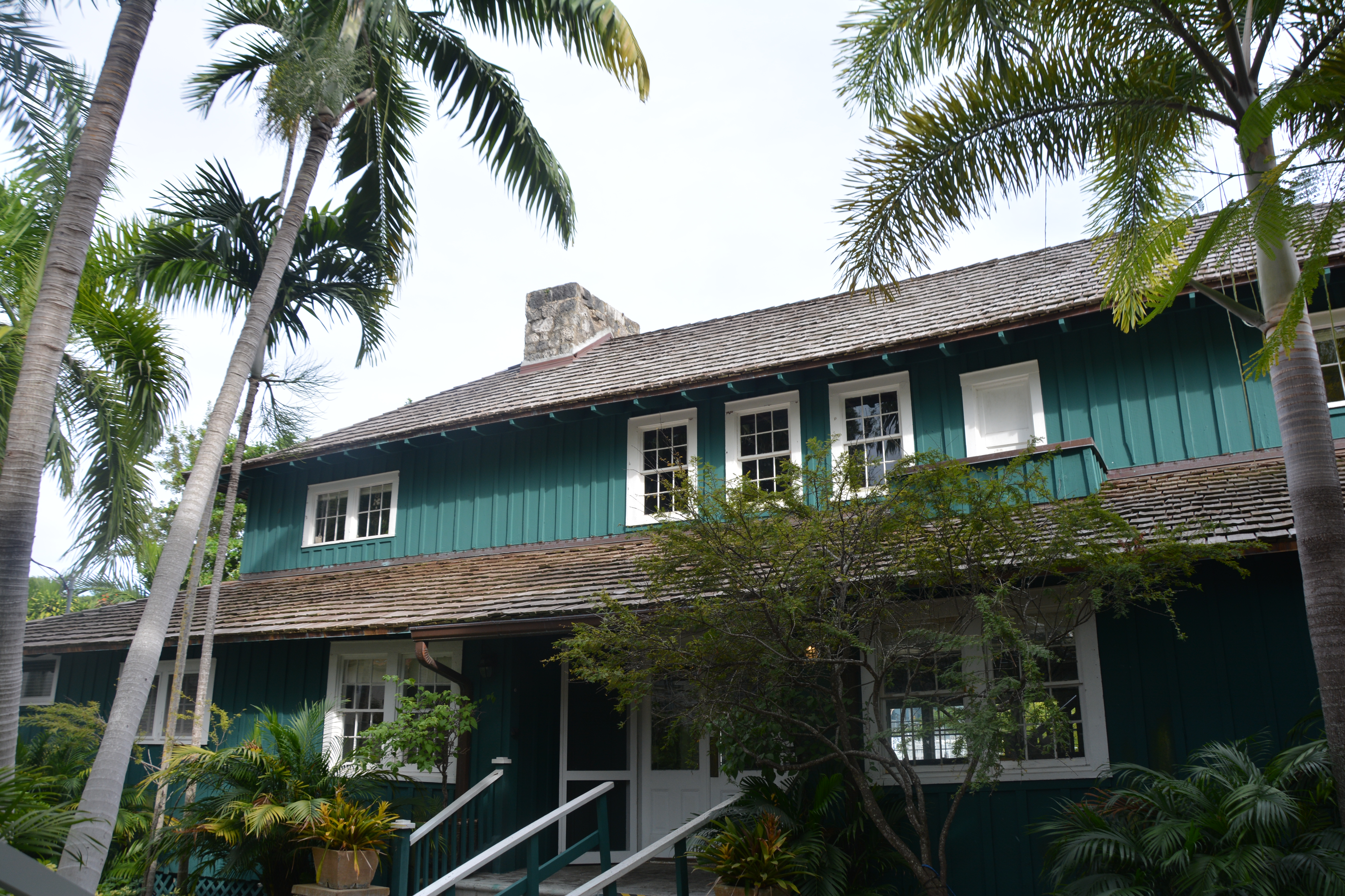 Two-story teal wooden building with white-trimmed windows surrounded by palm trees.