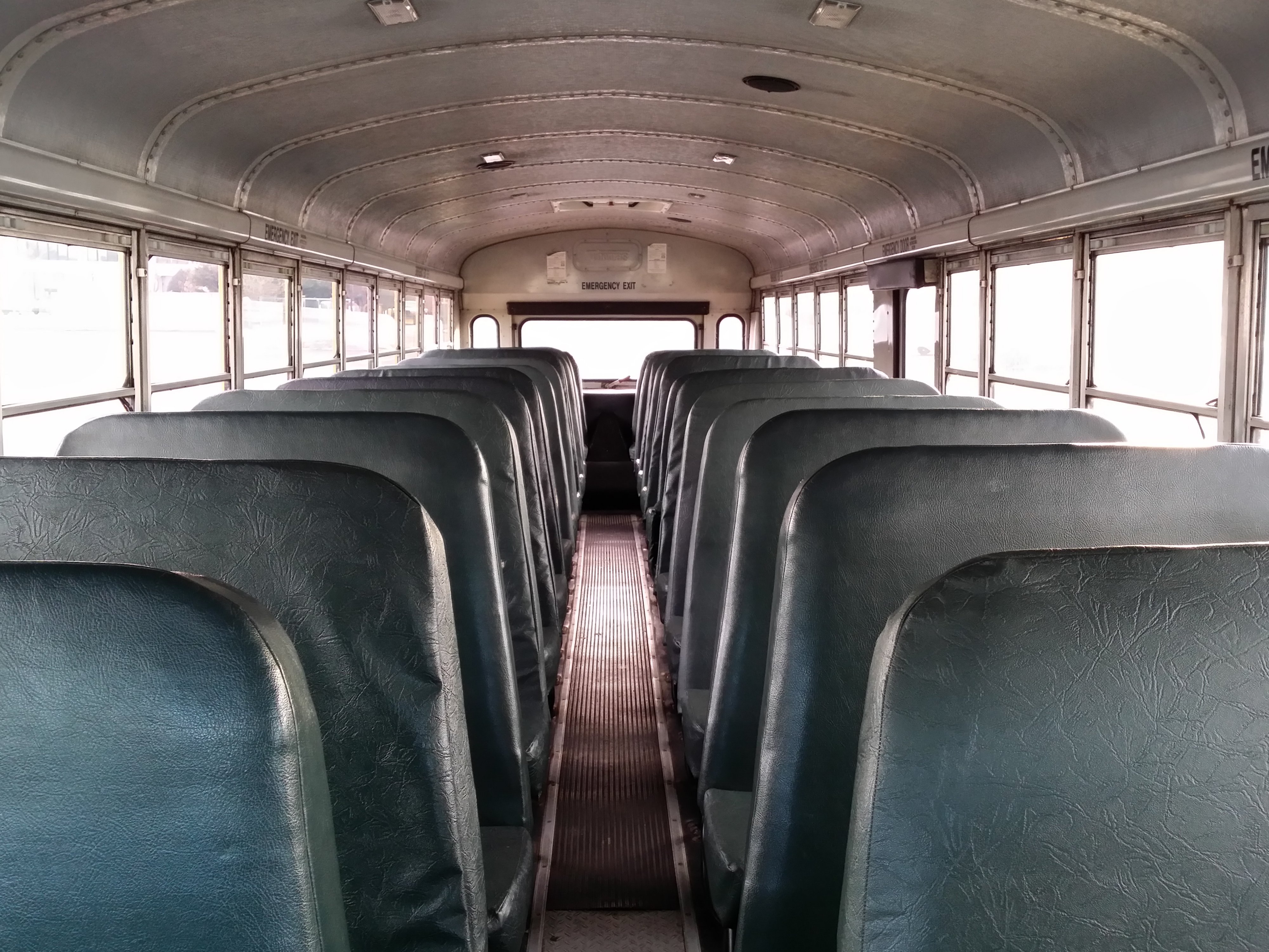 Empty school bus interior with rows of green vinyl bench seats and a center aisle.