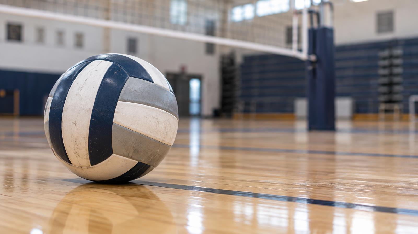 A volleyball resting on a hardwood gymnasium floor near the net.
