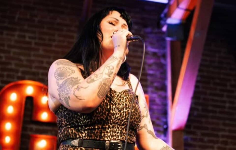 A woman with tattoos sings into a microphone on a stage.