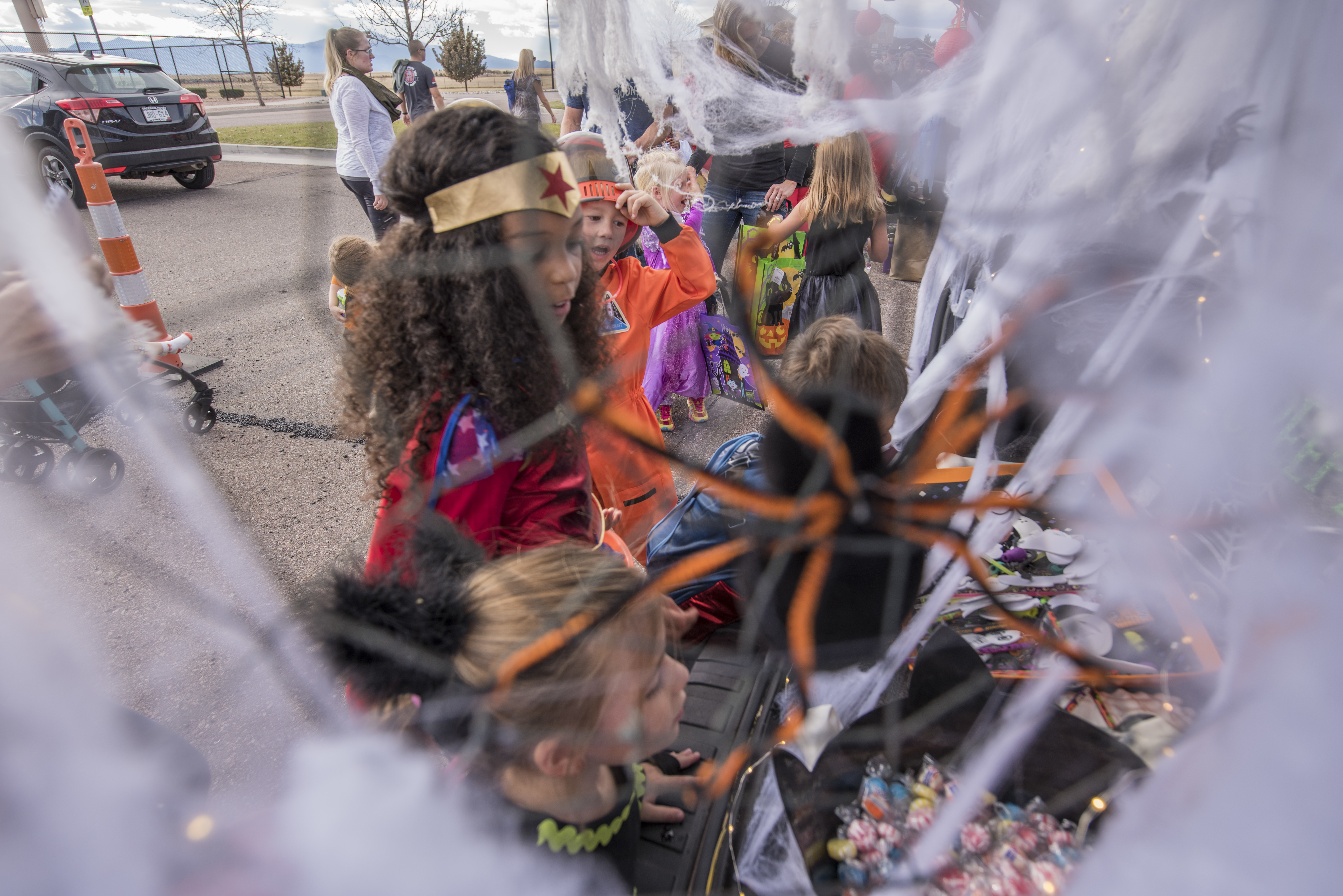 Children in Halloween costumes grabbing candy from decorated car trunks at an outdoor event.