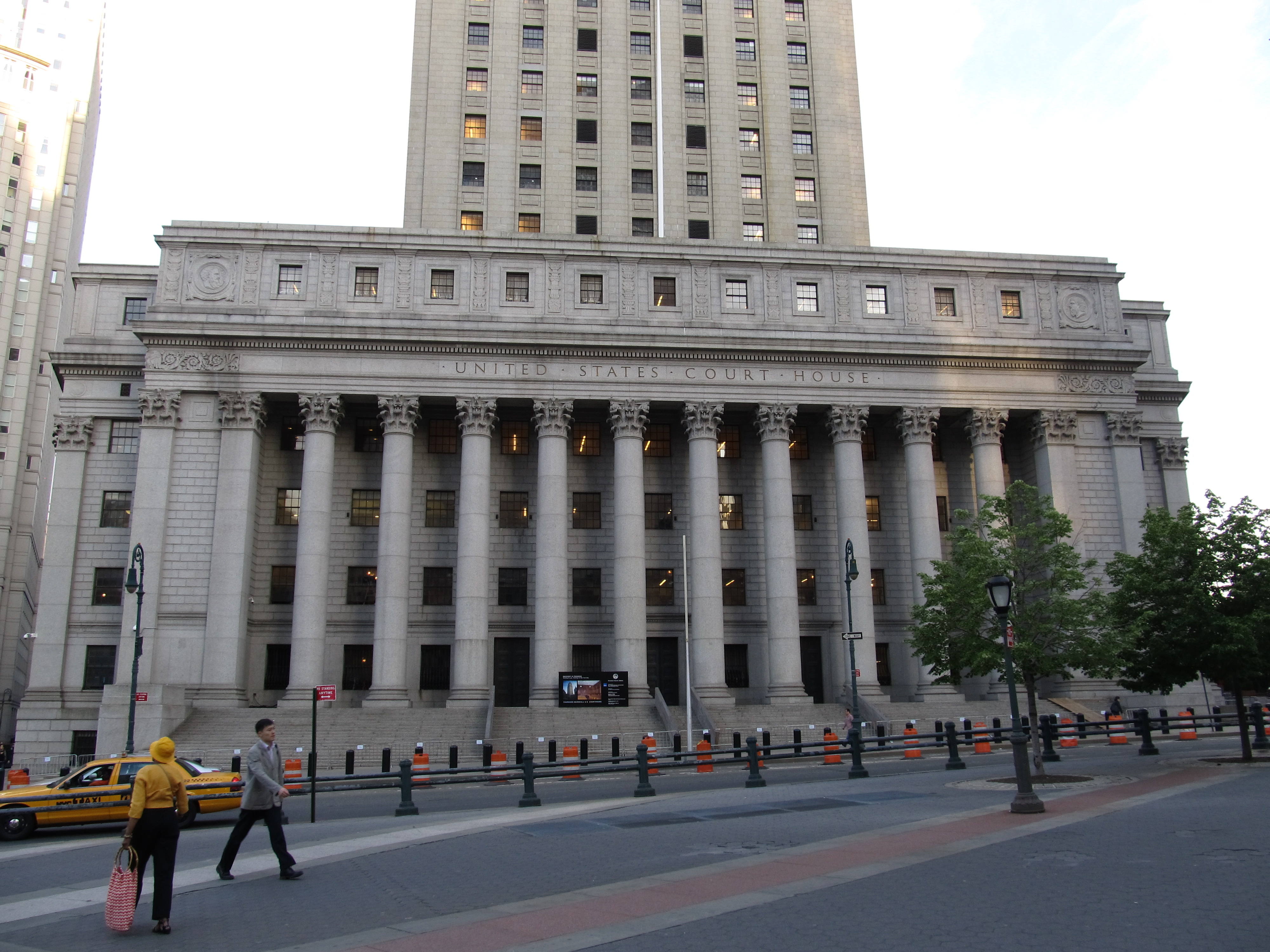 Neoclassical courthouse facade with large columns and 'United States Court House' inscription, pedestrians and yellow taxi on street.
