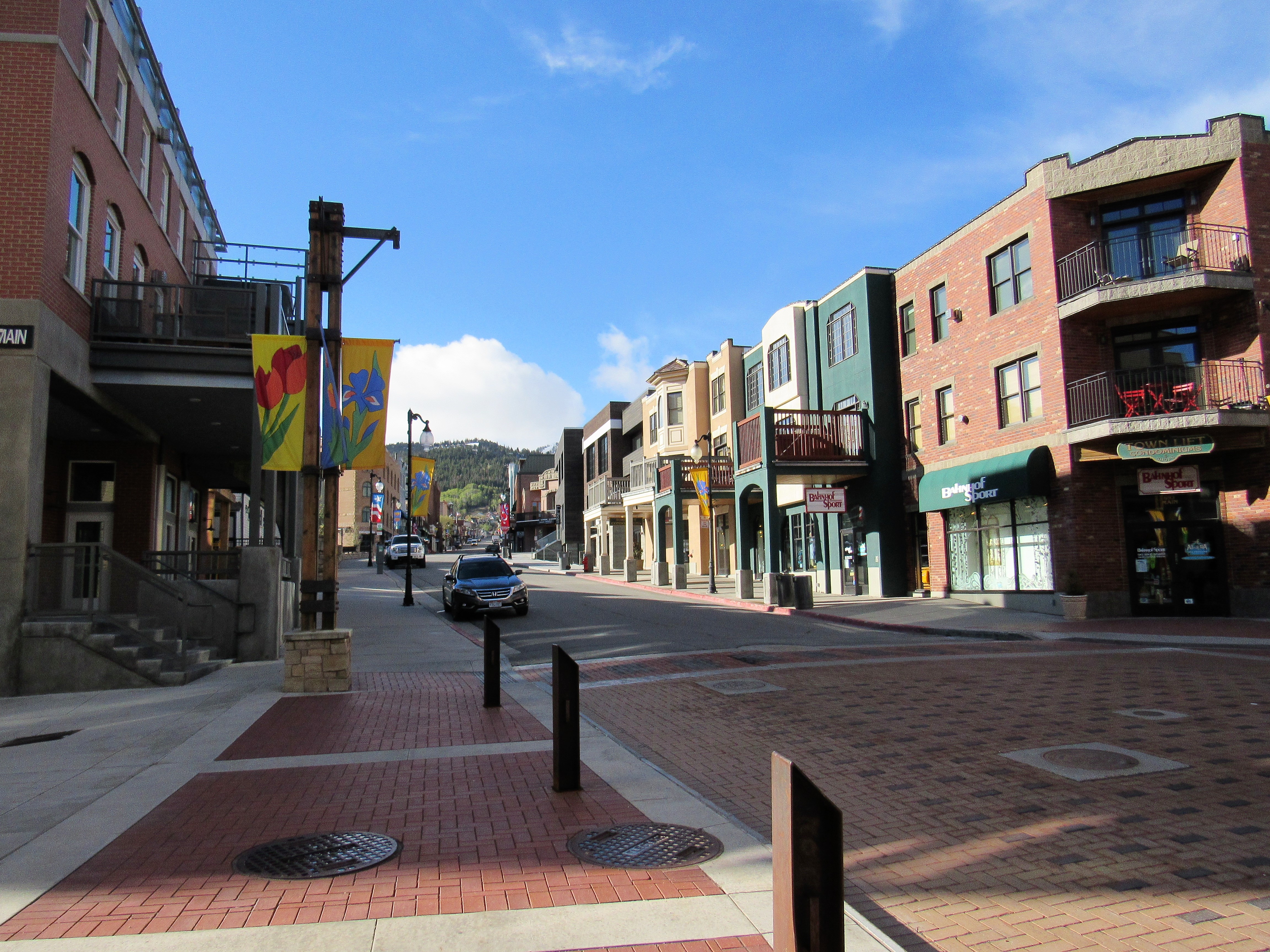 Brick-paved pedestrian street lined with historic storefronts, banners, and bollards, hills behind.