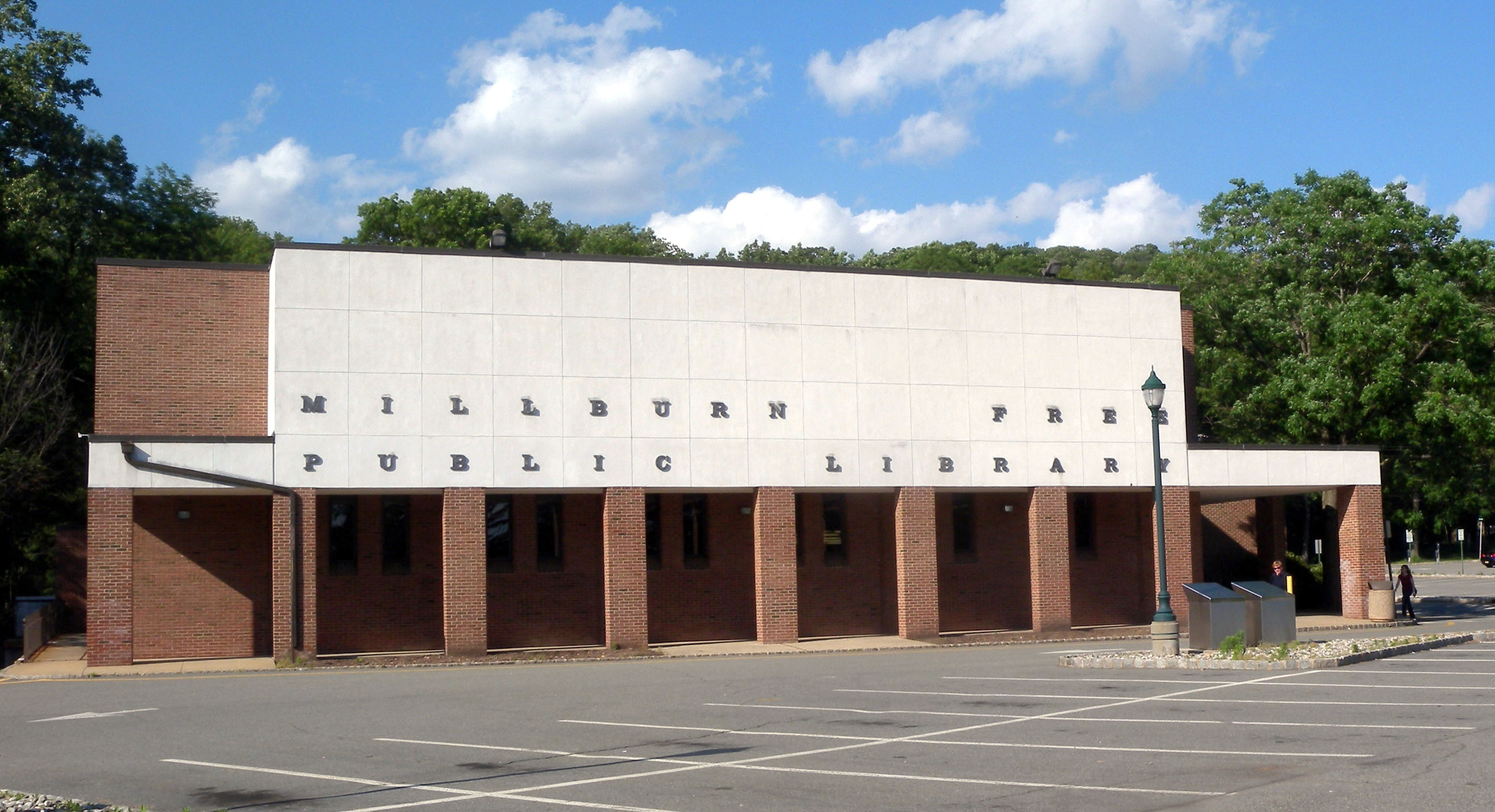 Exterior of a brick and white-panel public library building on a sunny day.