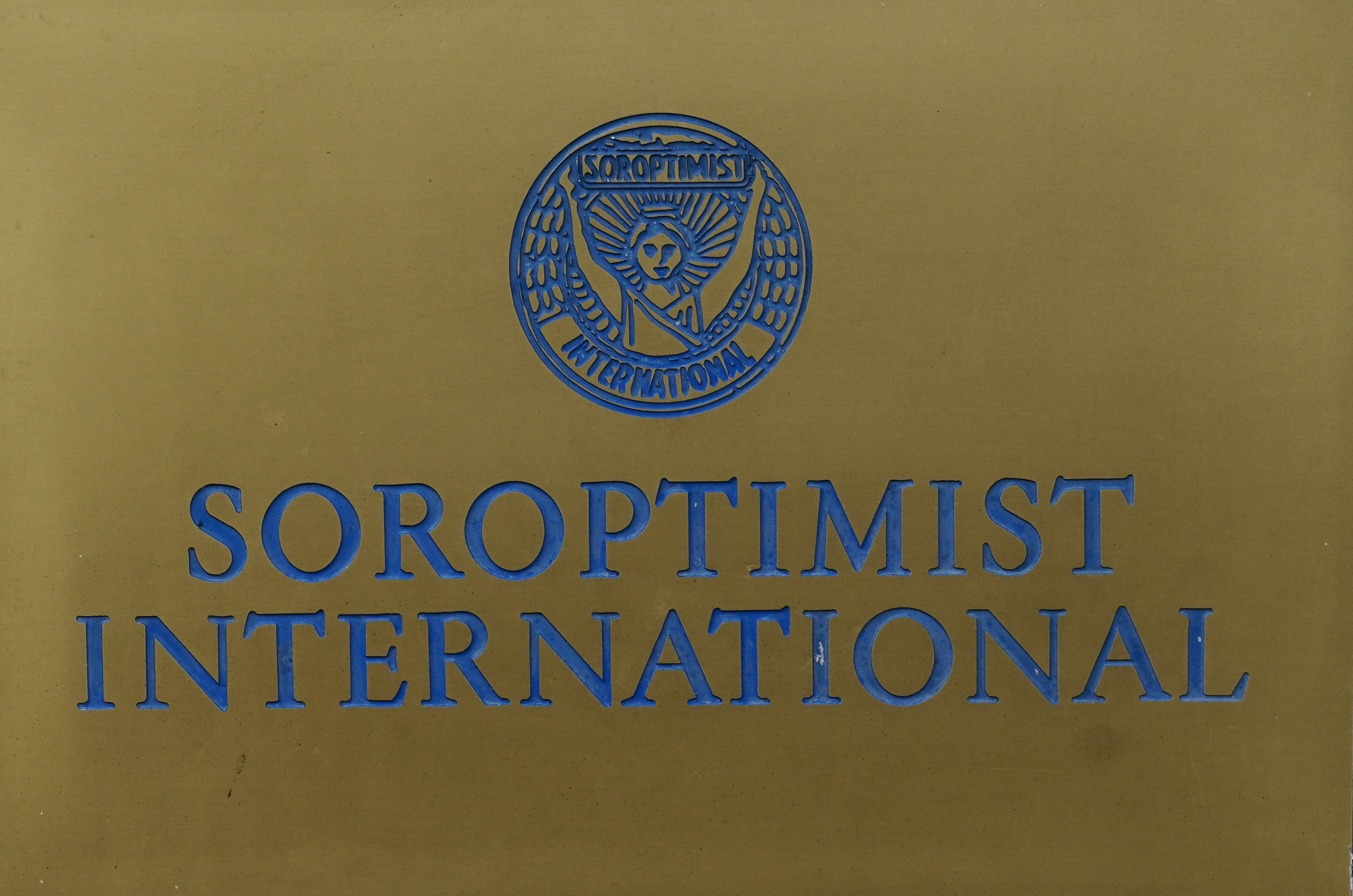 Gold plaque with blue Soroptimist International lettering and a circular emblem featuring a winged figure.