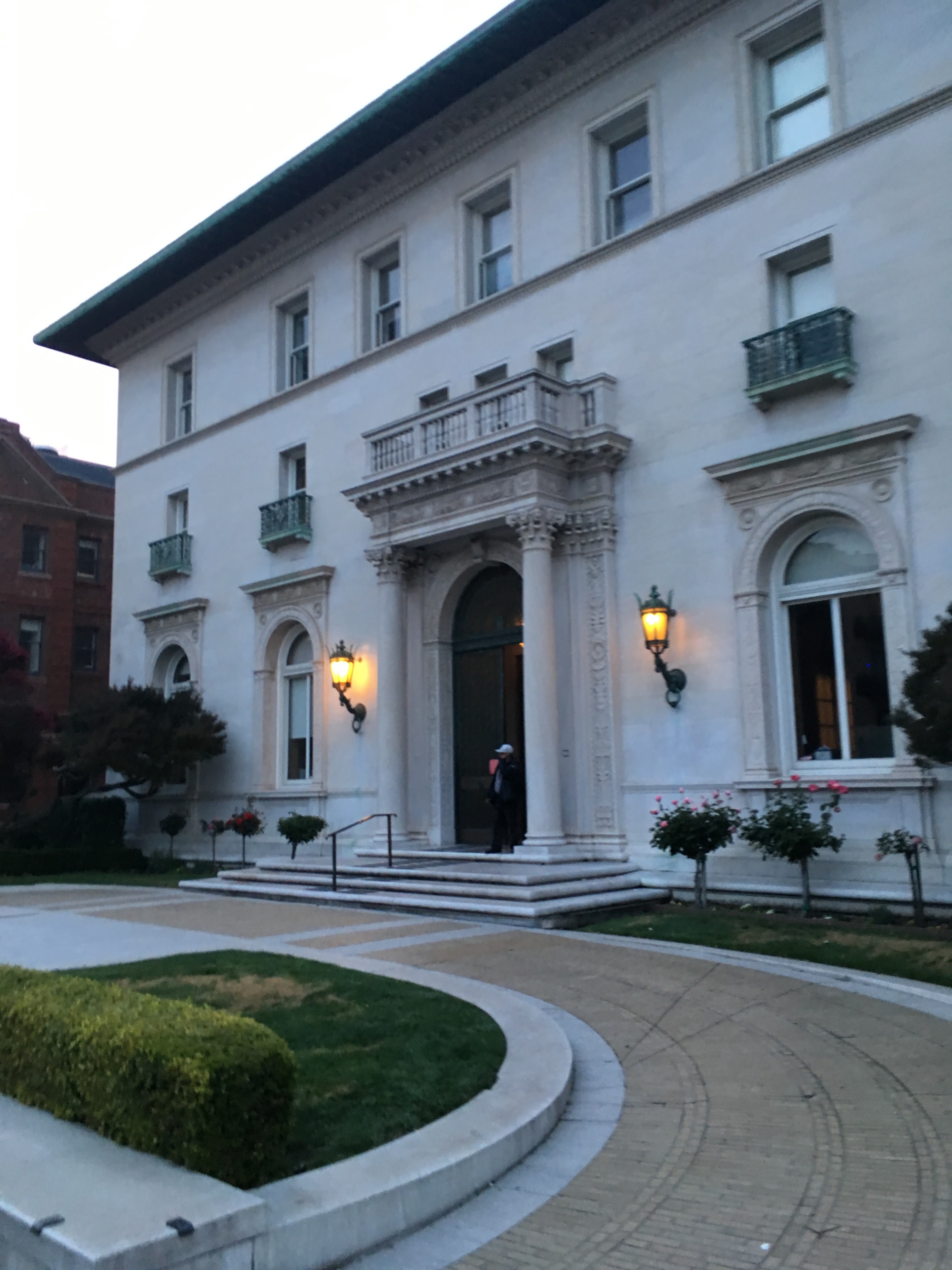 White neoclassical school building with columns and lantern lights at dusk.