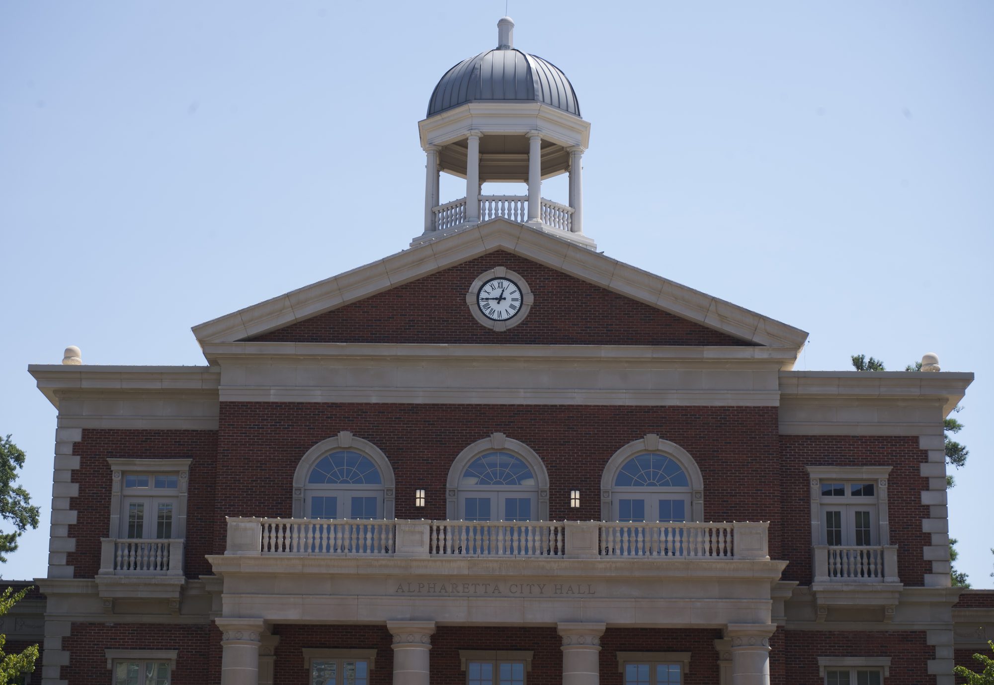 Red brick government building with domed cupola, clock, and arched windows.
