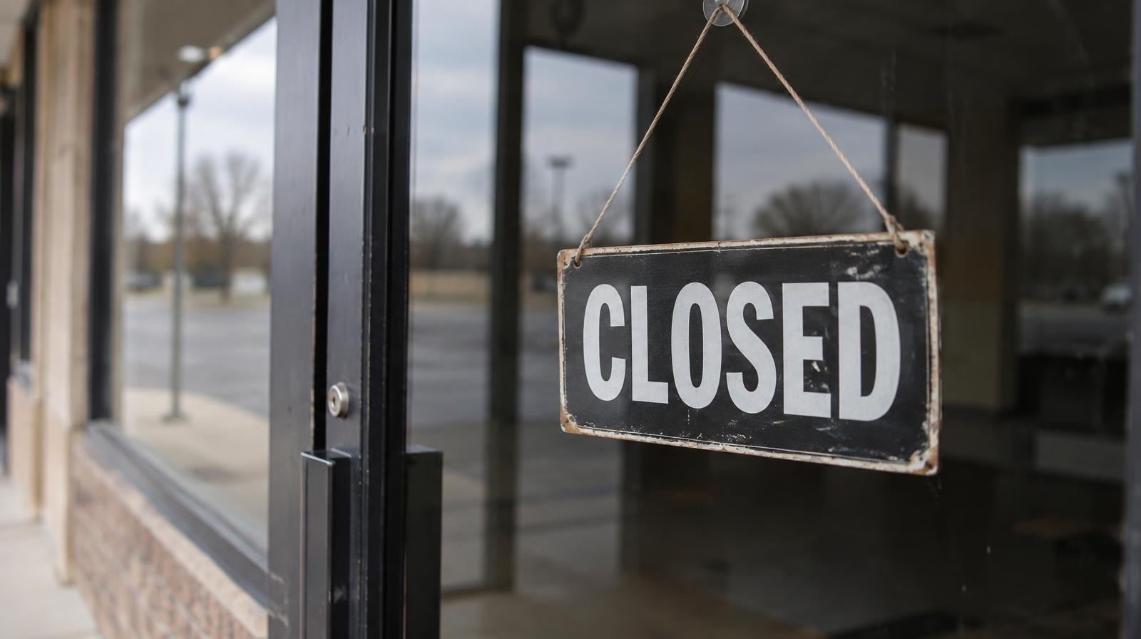 A closed sign hanging in the glass door of a darkened storefront.