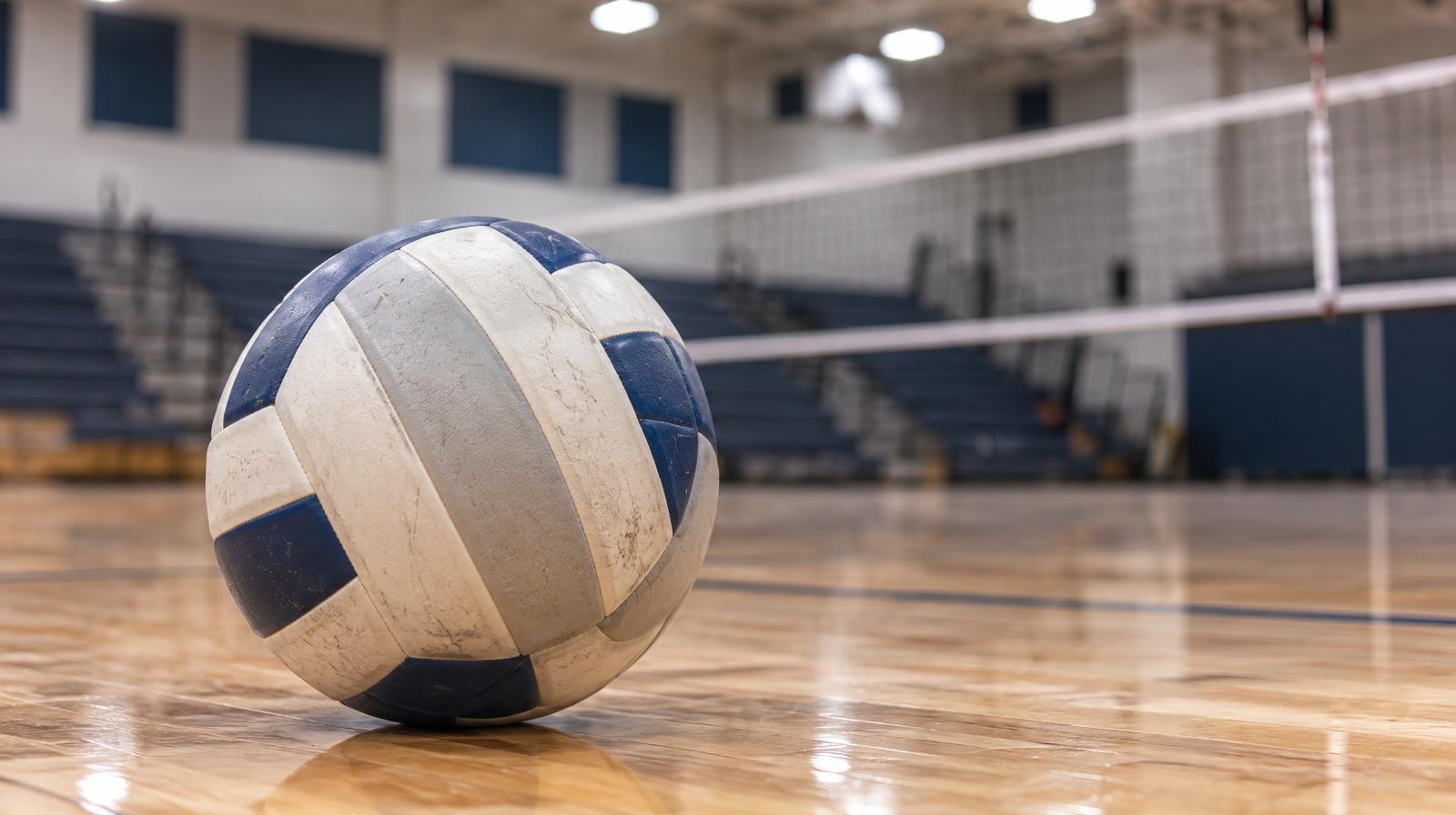 A volleyball resting on a hardwood gymnasium floor near the net.