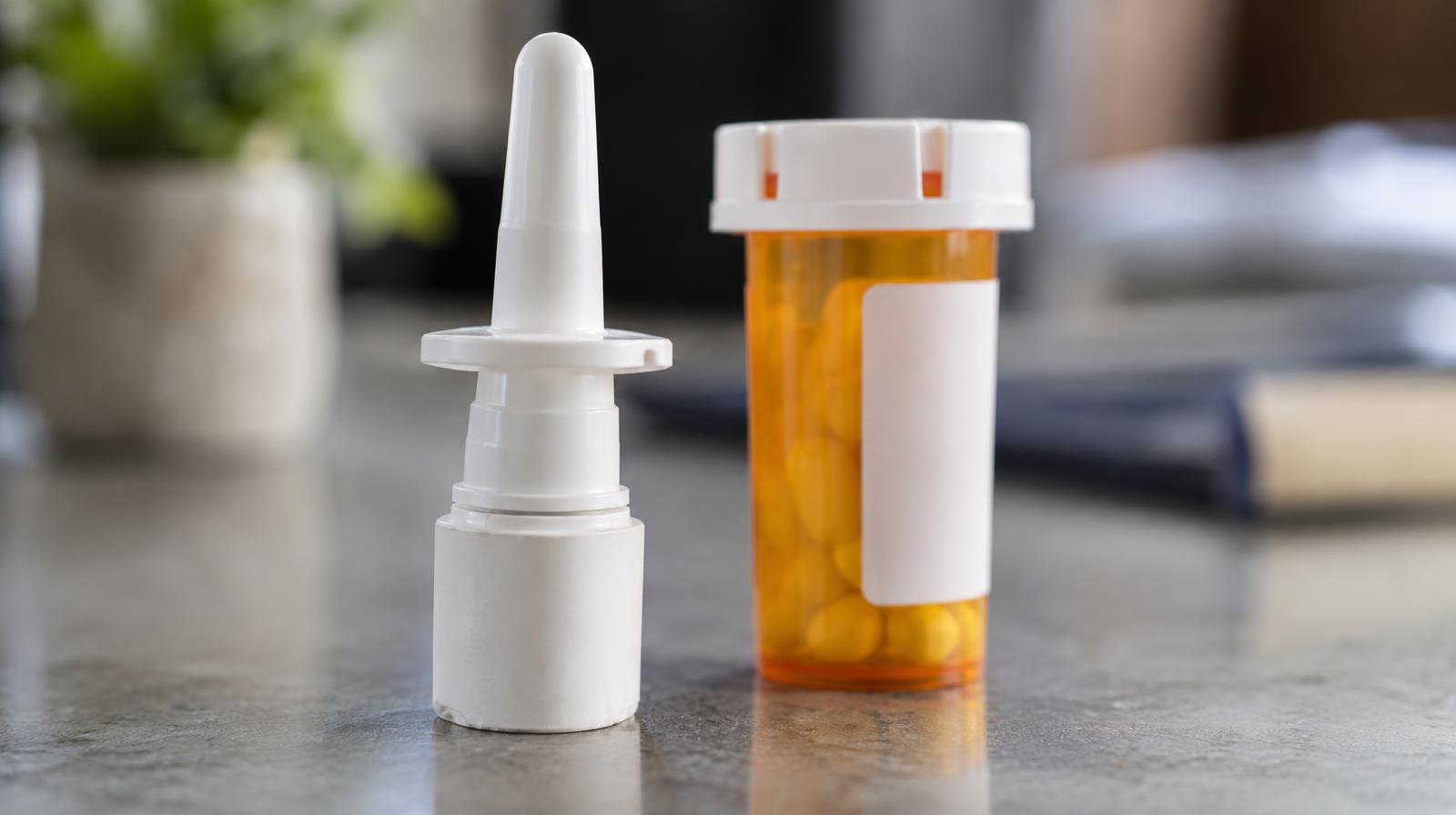 Naloxone nasal spray device next to an orange prescription pill bottle on a flat surface.