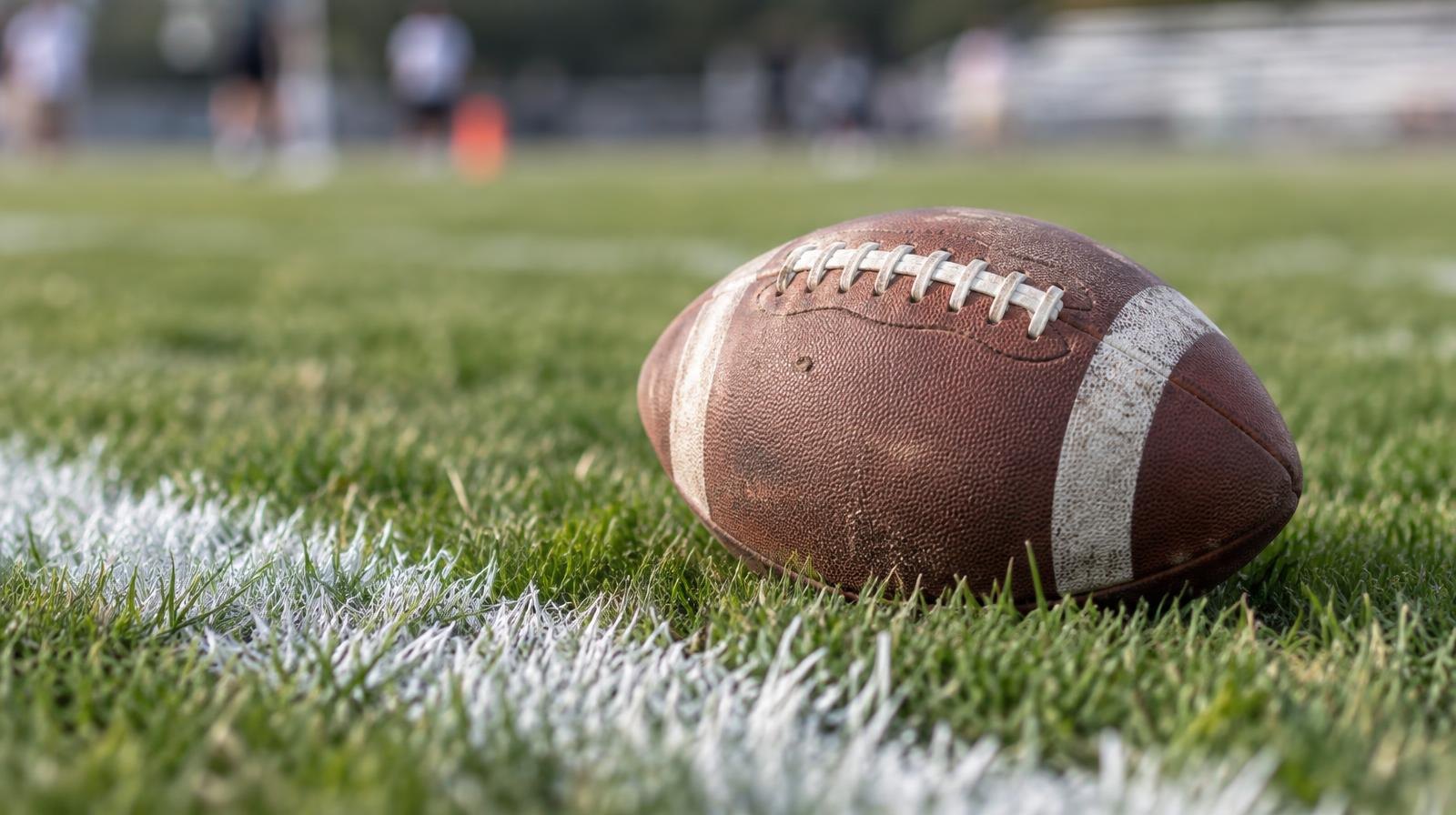 An American football resting on green grass beside a white painted yard line.