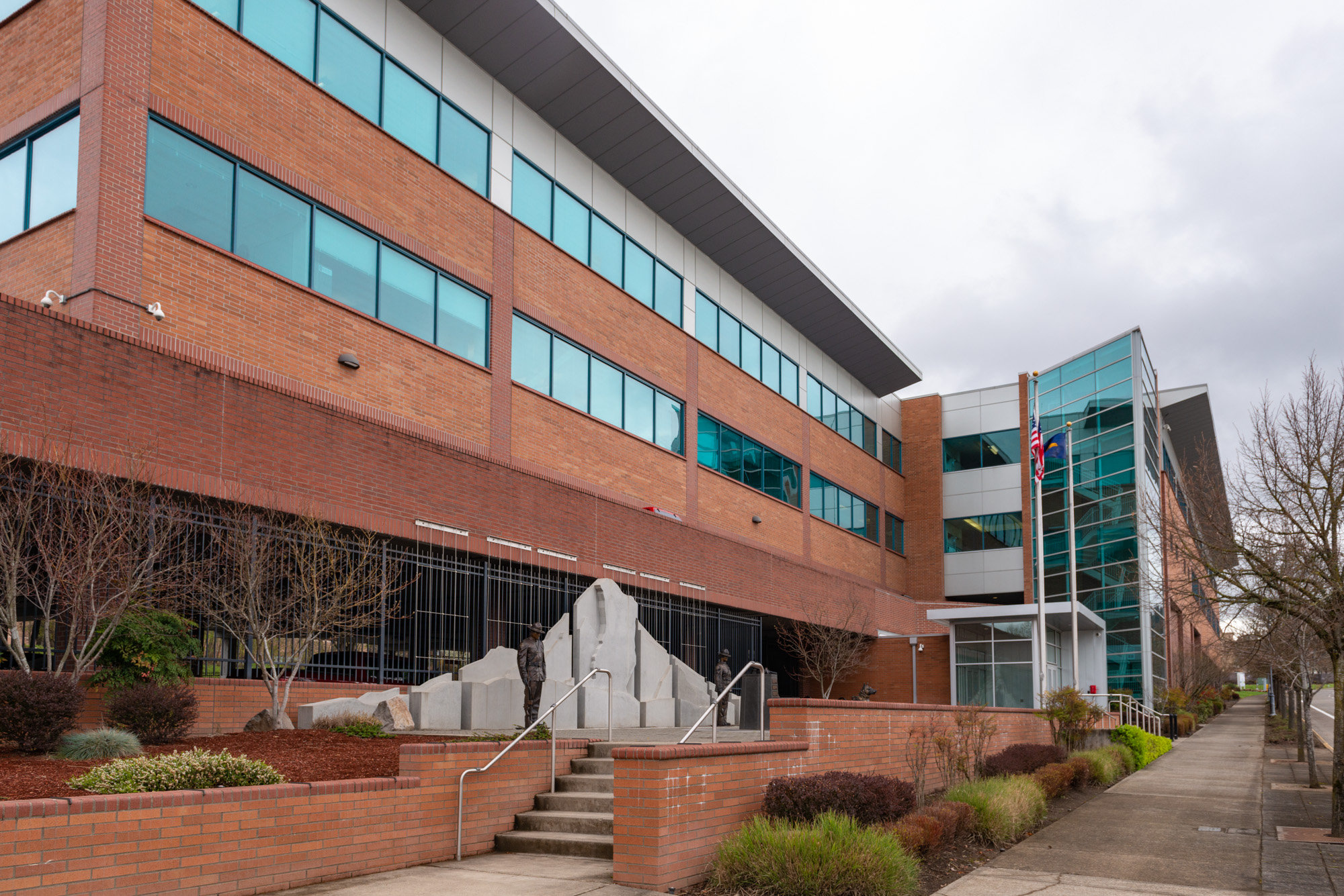 Multi-story red brick and glass office building with flagpole and stone sculptures at the entrance.