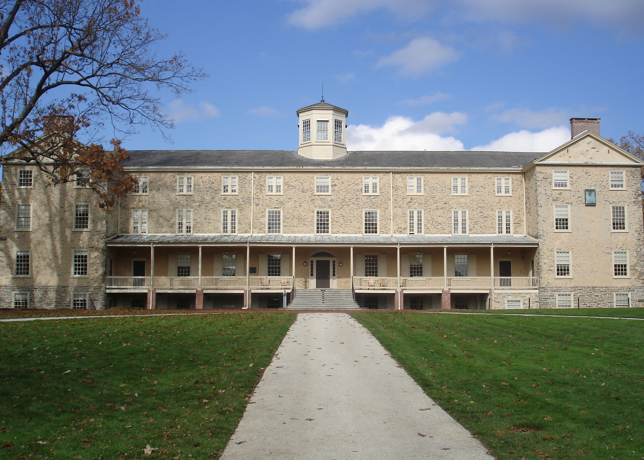 Stone academic building with central cupola and covered porch on a green lawn.