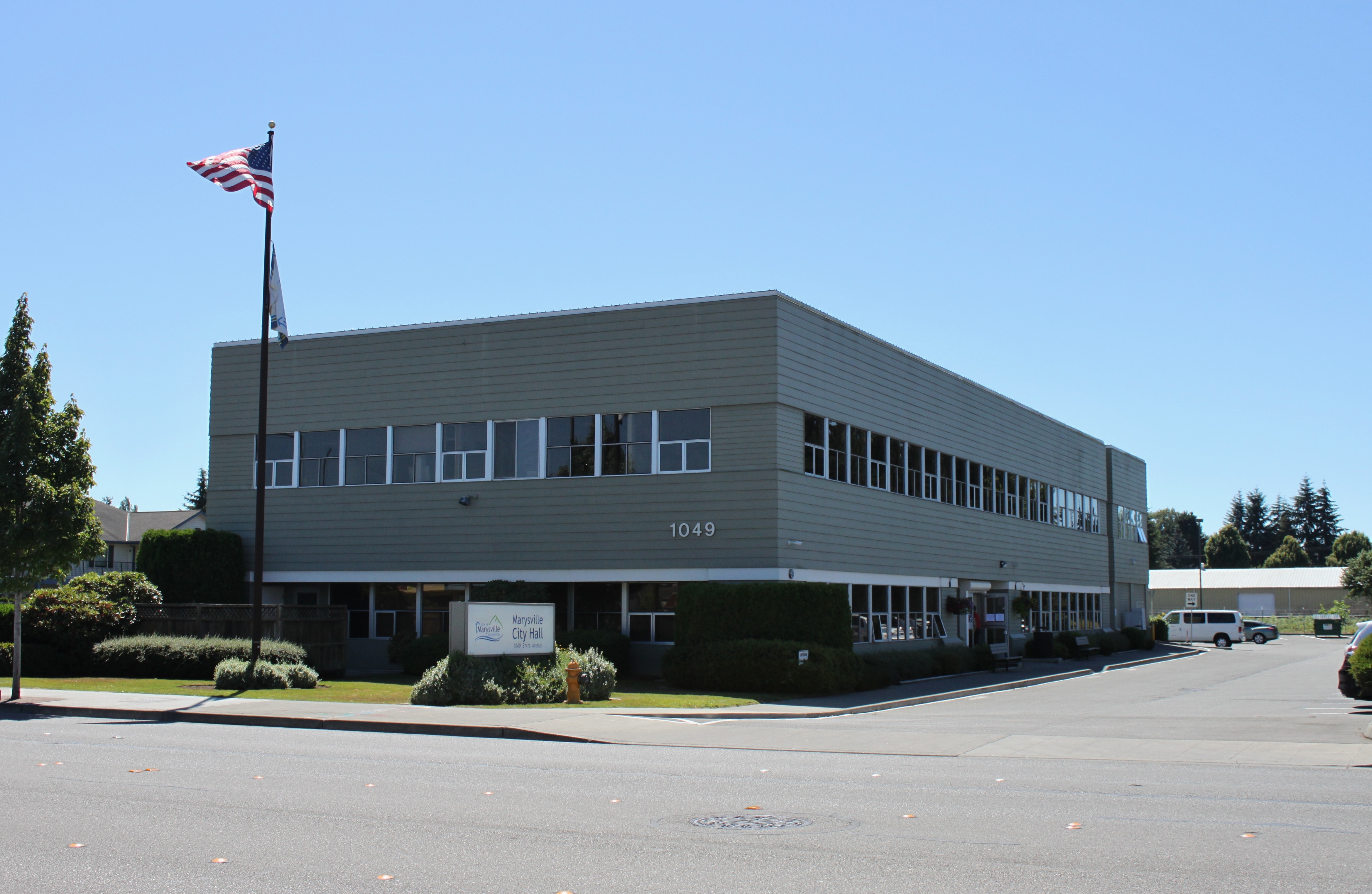 Two-story government building with an American flag on a pole out front.