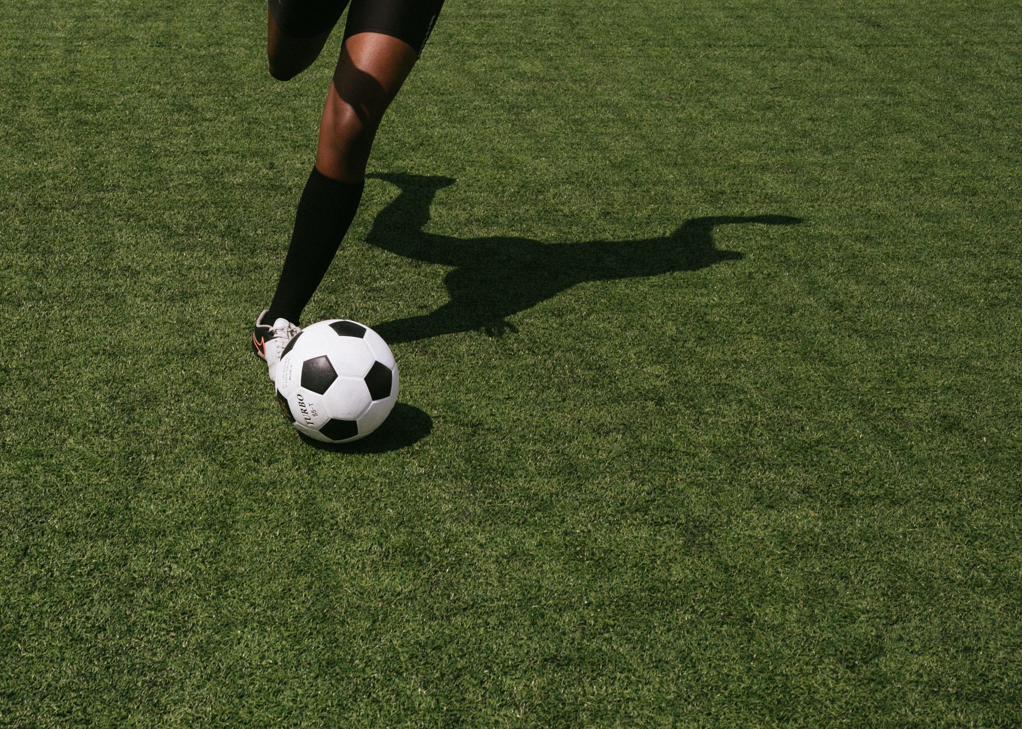 Faceless football player kicking ball on grass field of stadium during soccer match