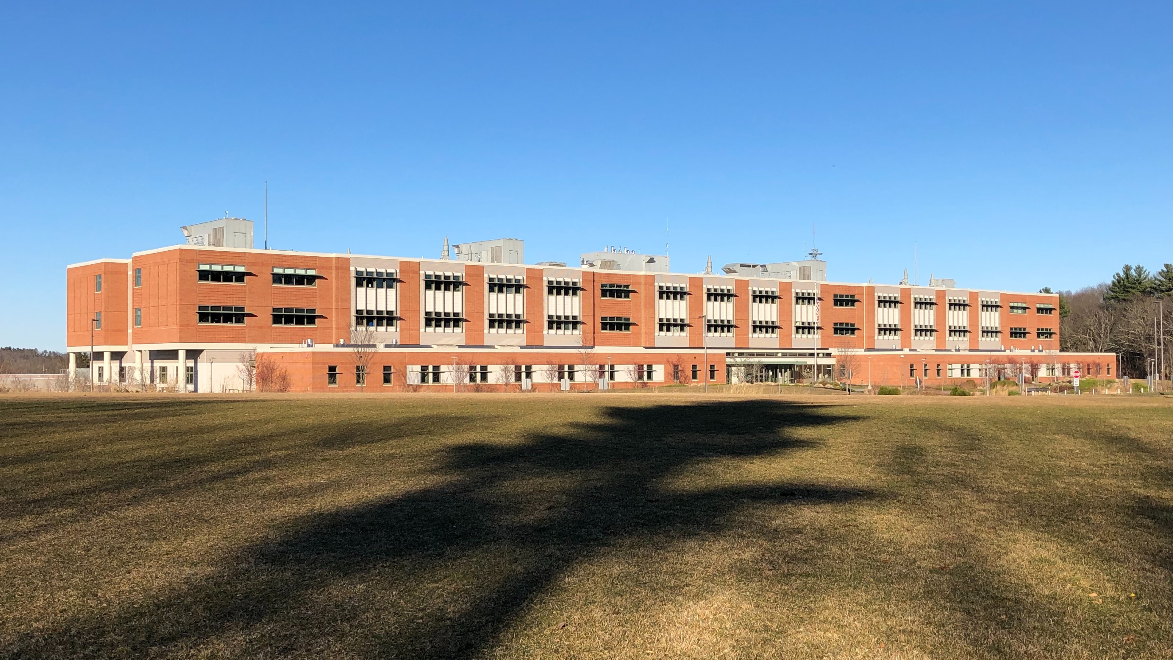 A large red brick school building viewed from across a wide green lawn under a blue sky.