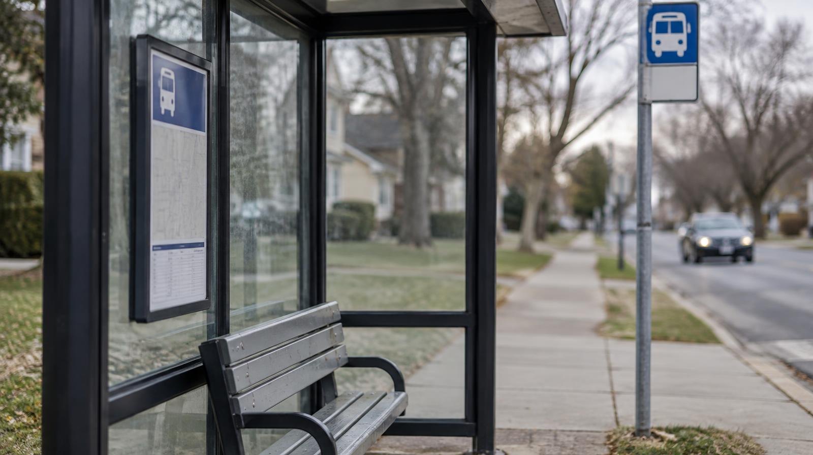 A bus stop shelter with a bench and route sign pole on a suburban sidewalk.