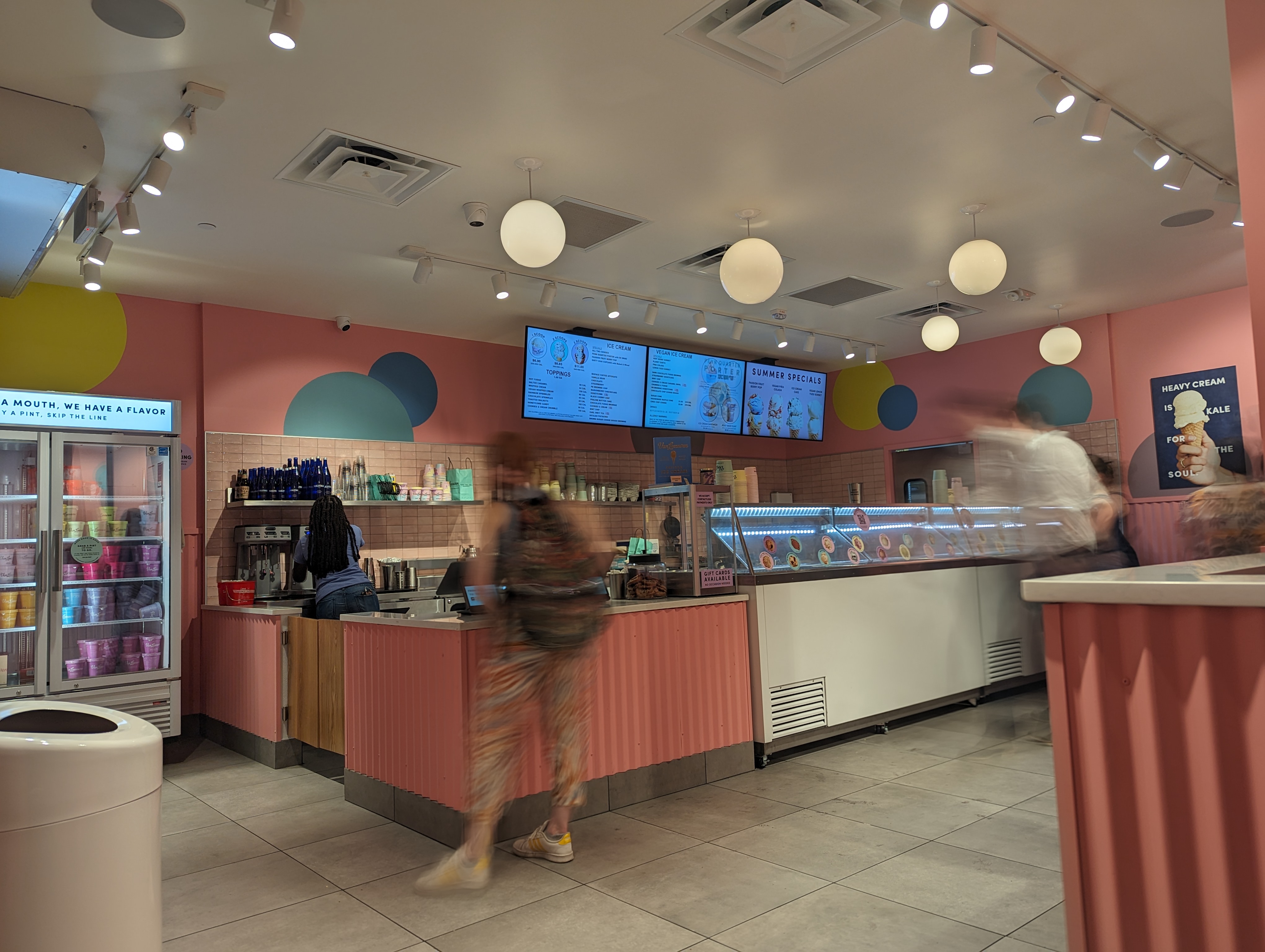 Inside a Van Leeuwen ice cream shop with pink counters, display case, and menu screens.
