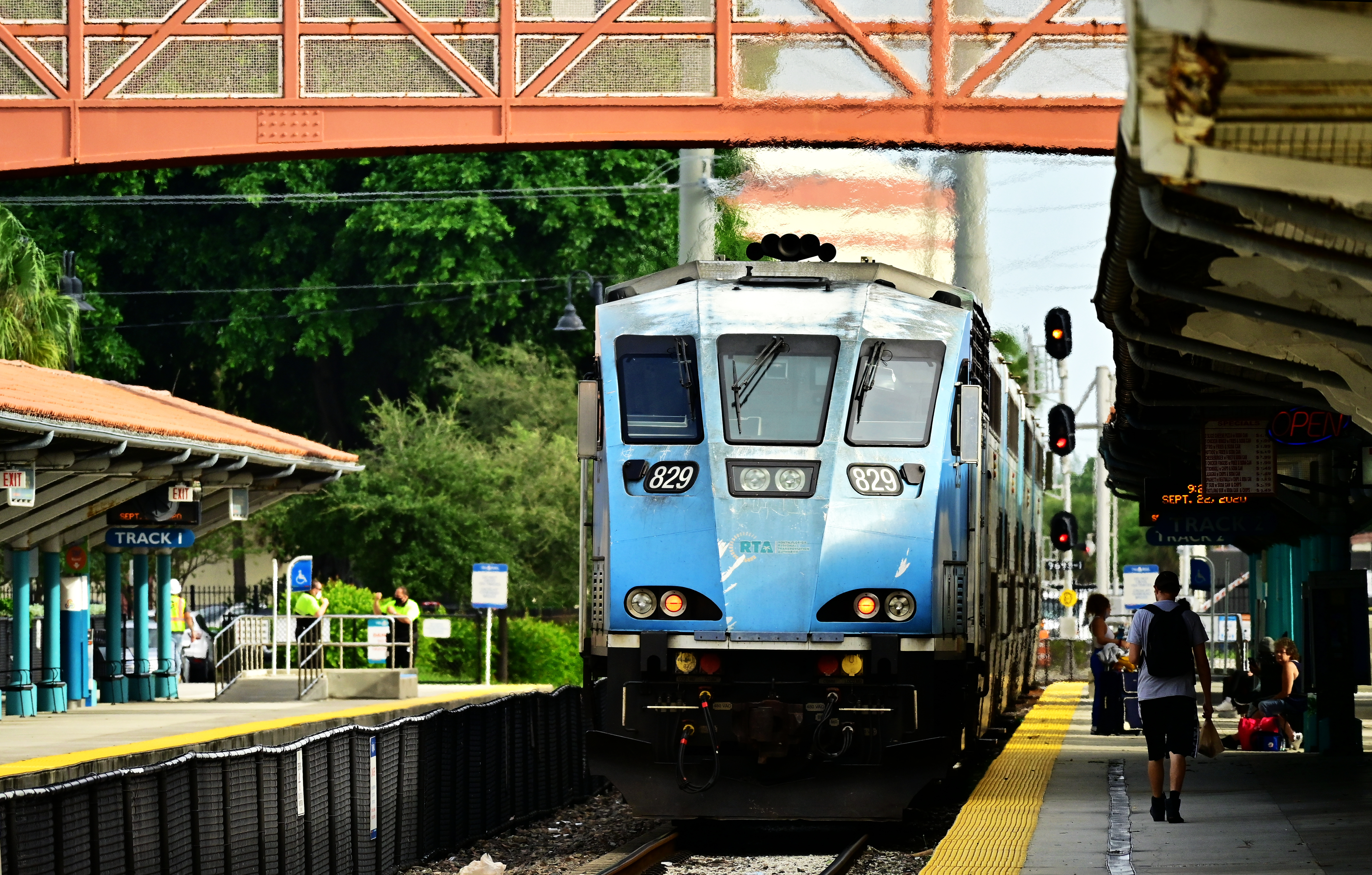 A blue commuter train arrives at a covered station platform with waiting passengers.