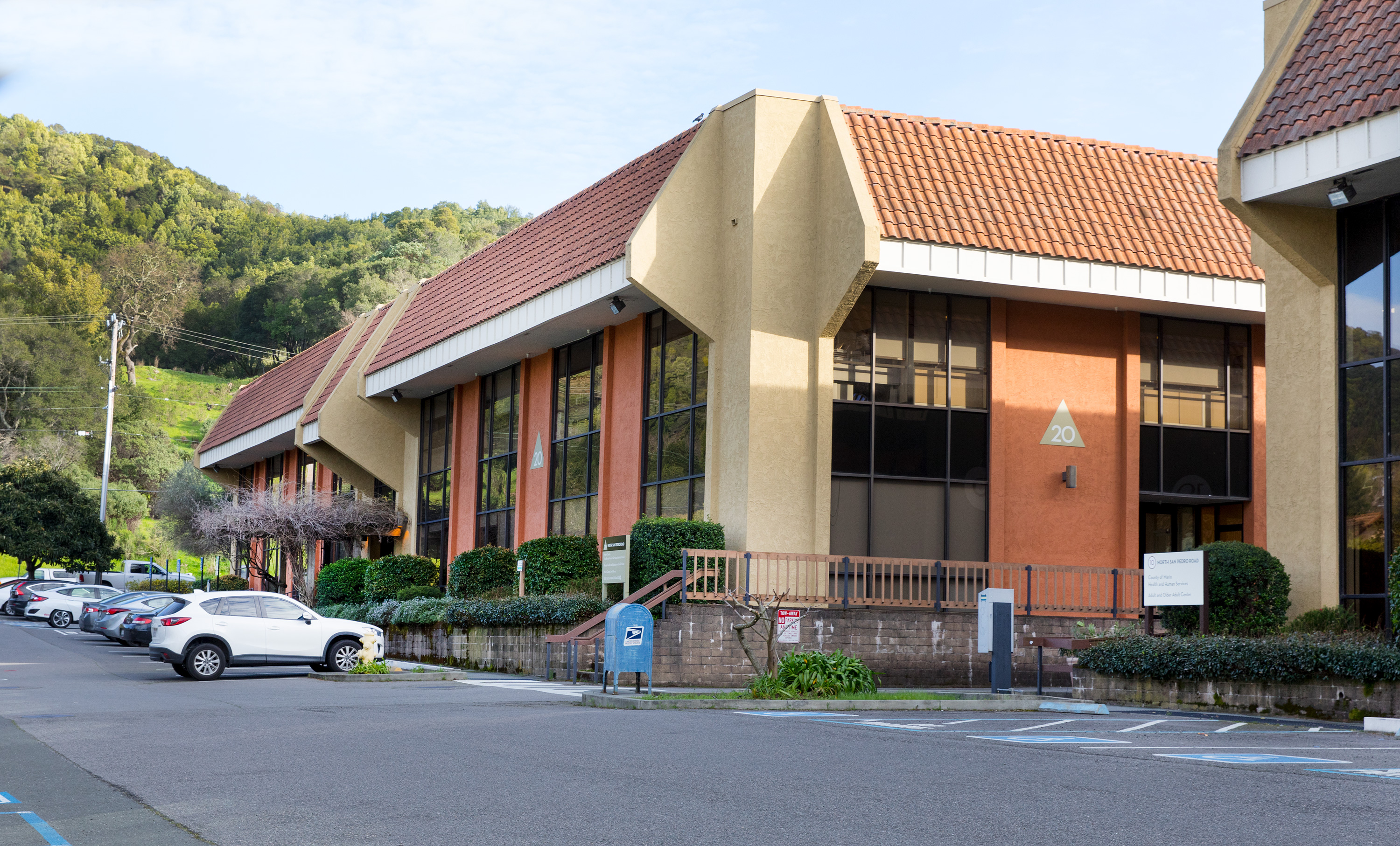 Multi-story government building with terracotta tile roof and tan stucco walls, parking lot in front.