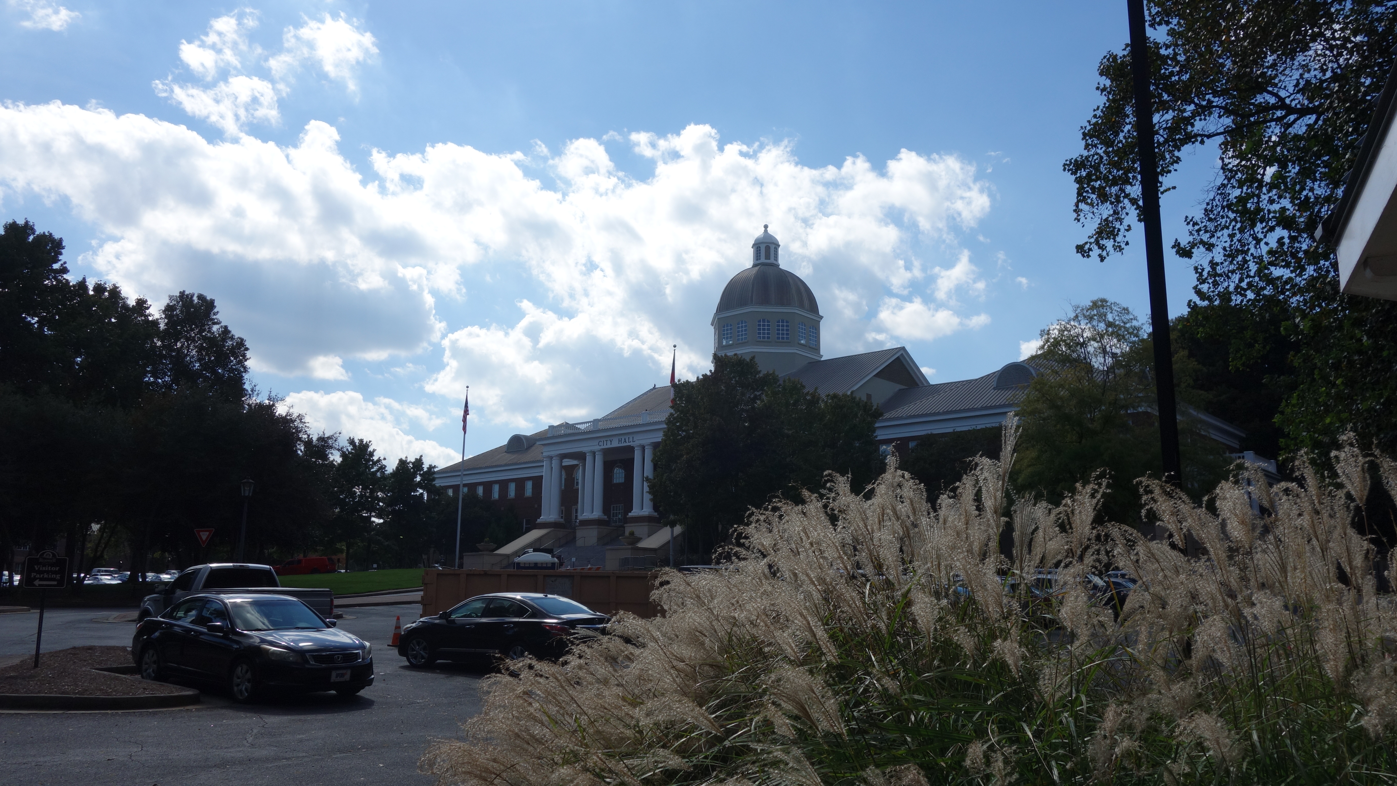 Front view of a brick government building with a dome and white columned entrance surrounded by trees.