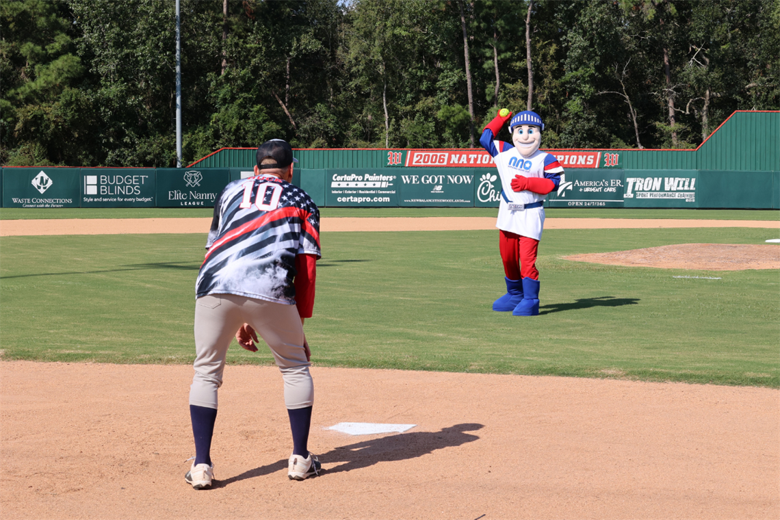 Man and mascot throw baseball on field.