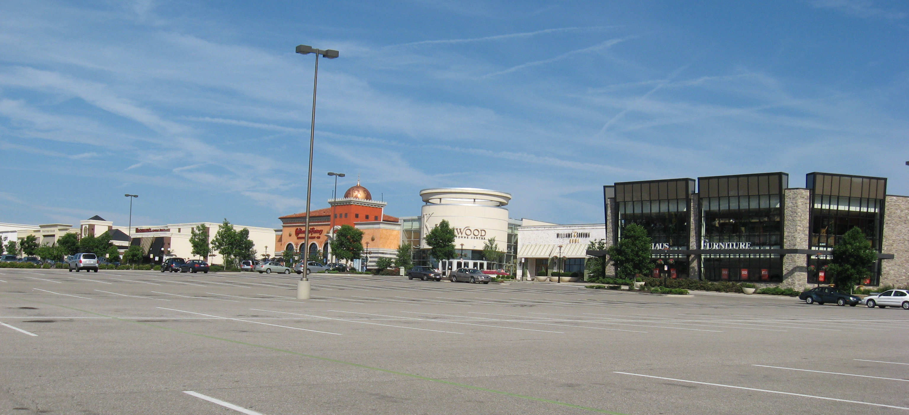 Large suburban shopping mall facade viewed across a parking lot under a blue sky.