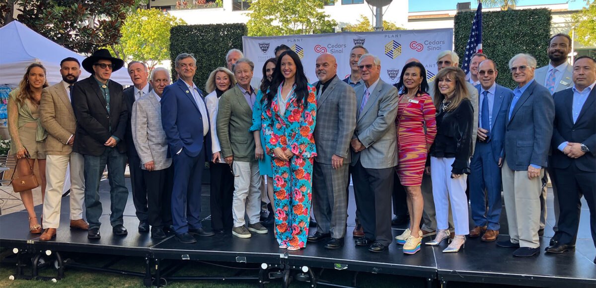 Group of approximately 20 people in formal attire posing on an outdoor stage at a garden event.