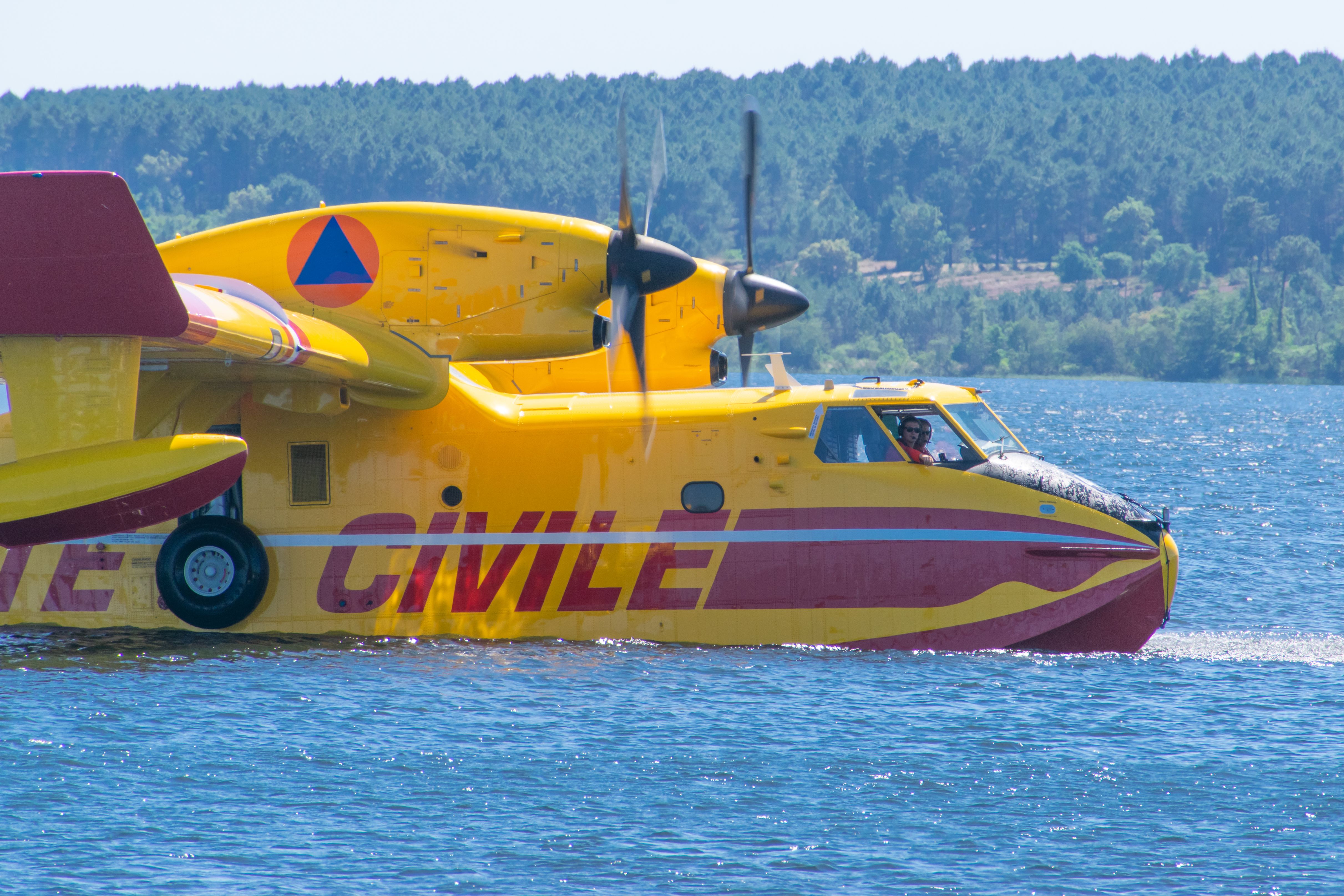 Yellow and red amphibious aircraft taxiing on a calm water surface.