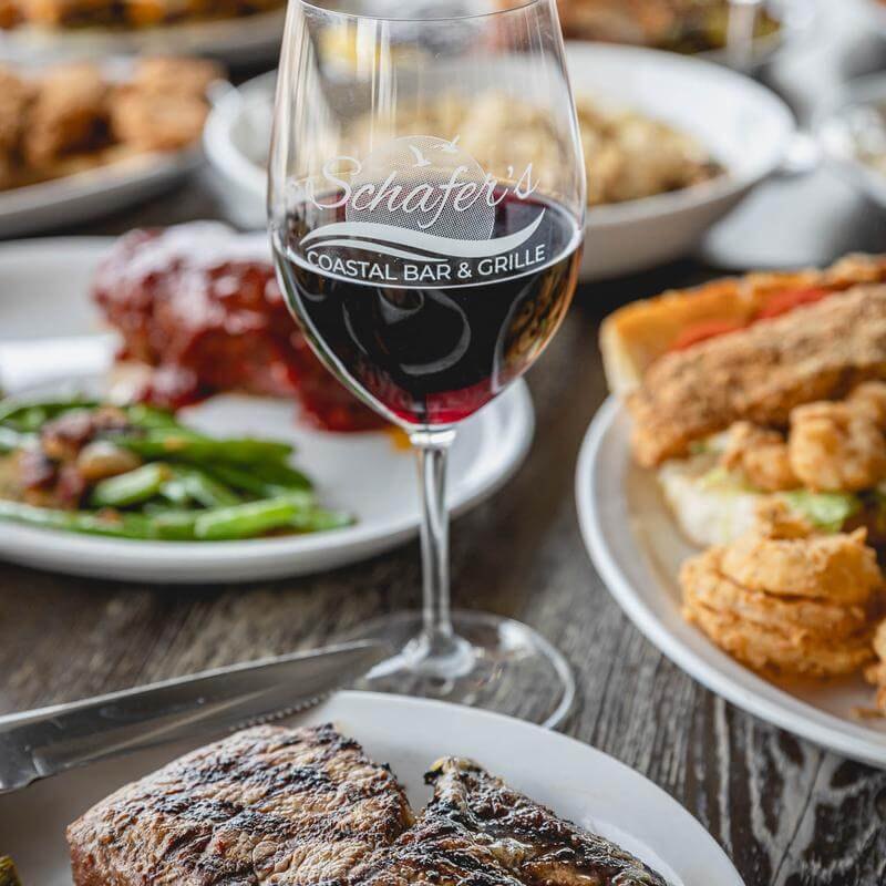 Branded wine glass and plated steak at a restaurant table with multiple dishes.