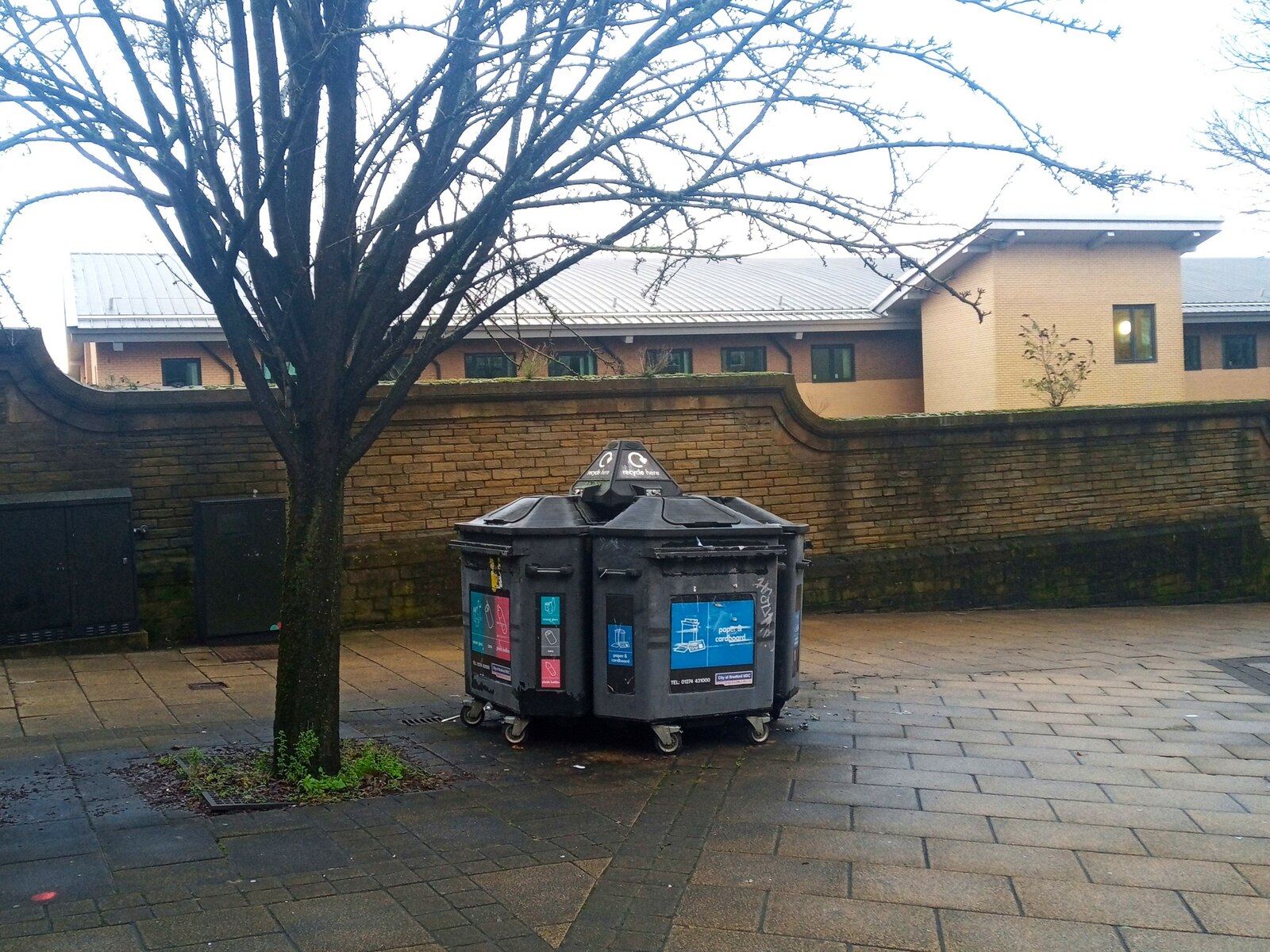 Multi-compartment recycling bin station with labeled sorting openings on a public plaza.