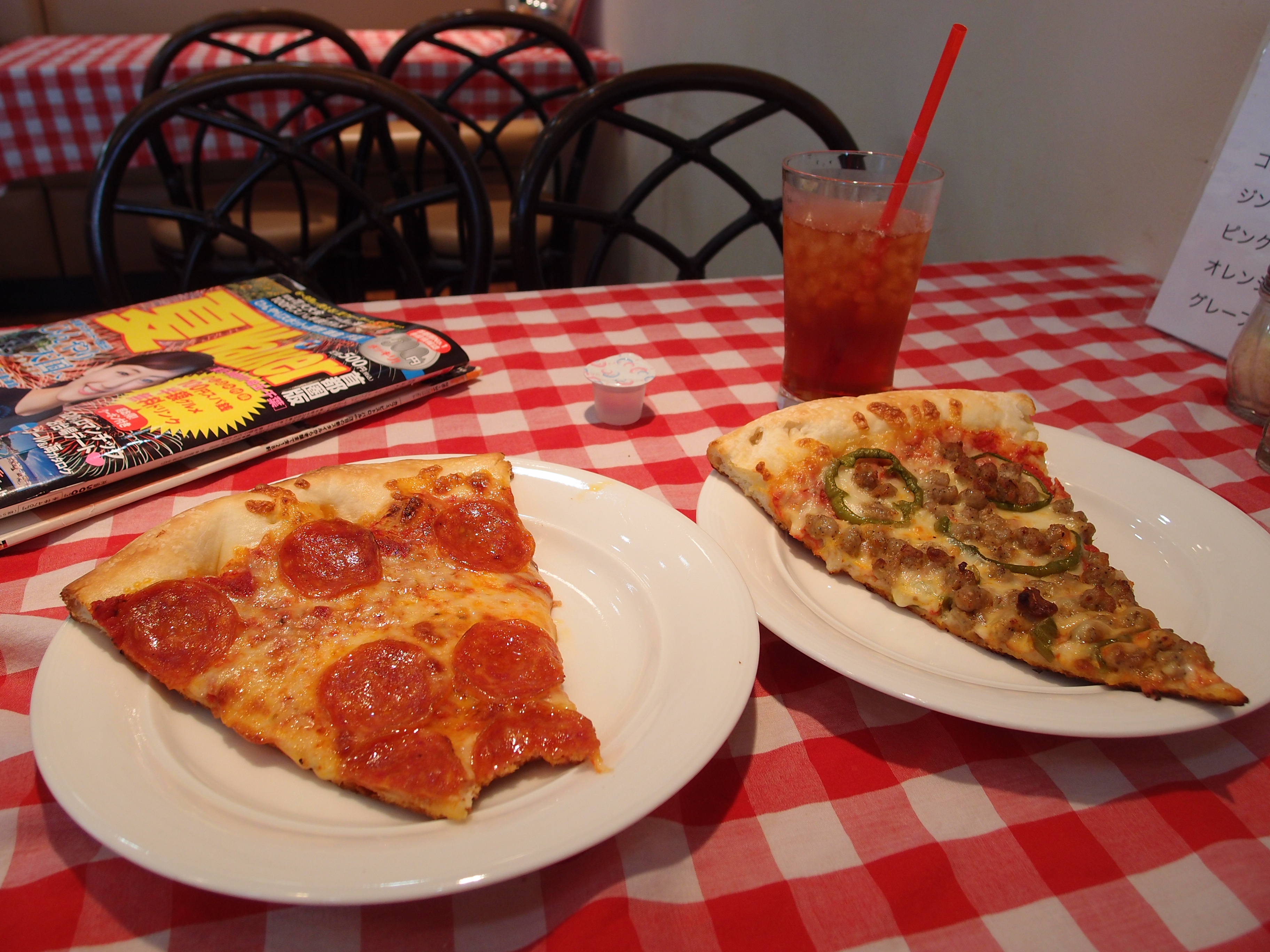 Two large pizza slices on white plates atop a checkered tablecloth.
