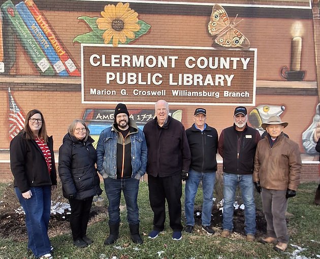 Group of seven people standing outside a library branch in front of a colorful mural.