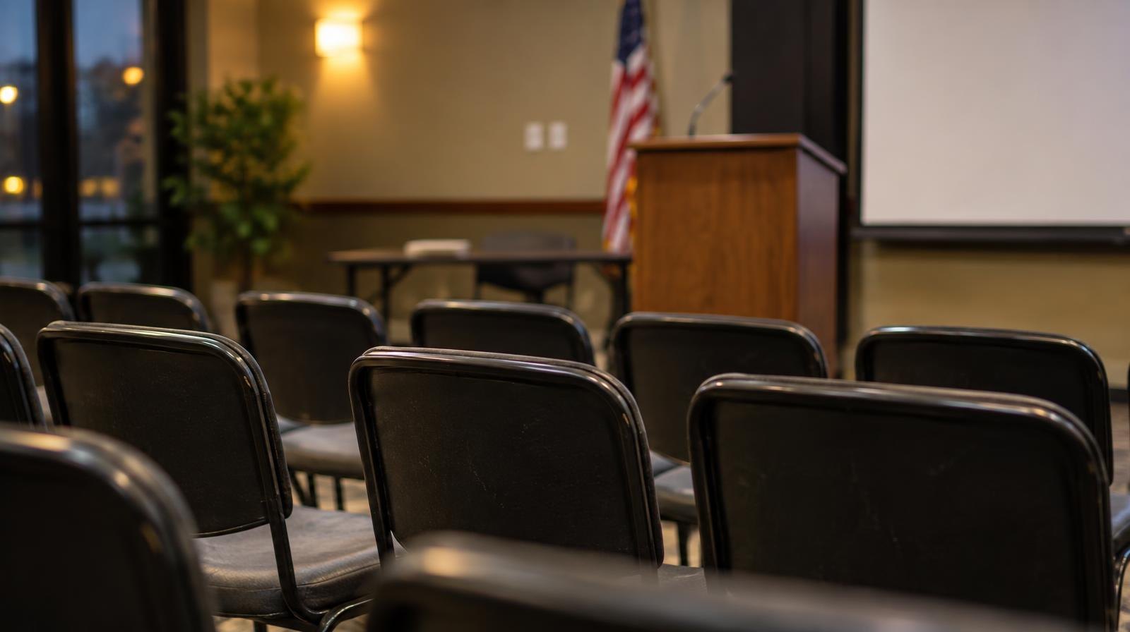 Empty chairs arranged in rows facing a podium in a meeting room.