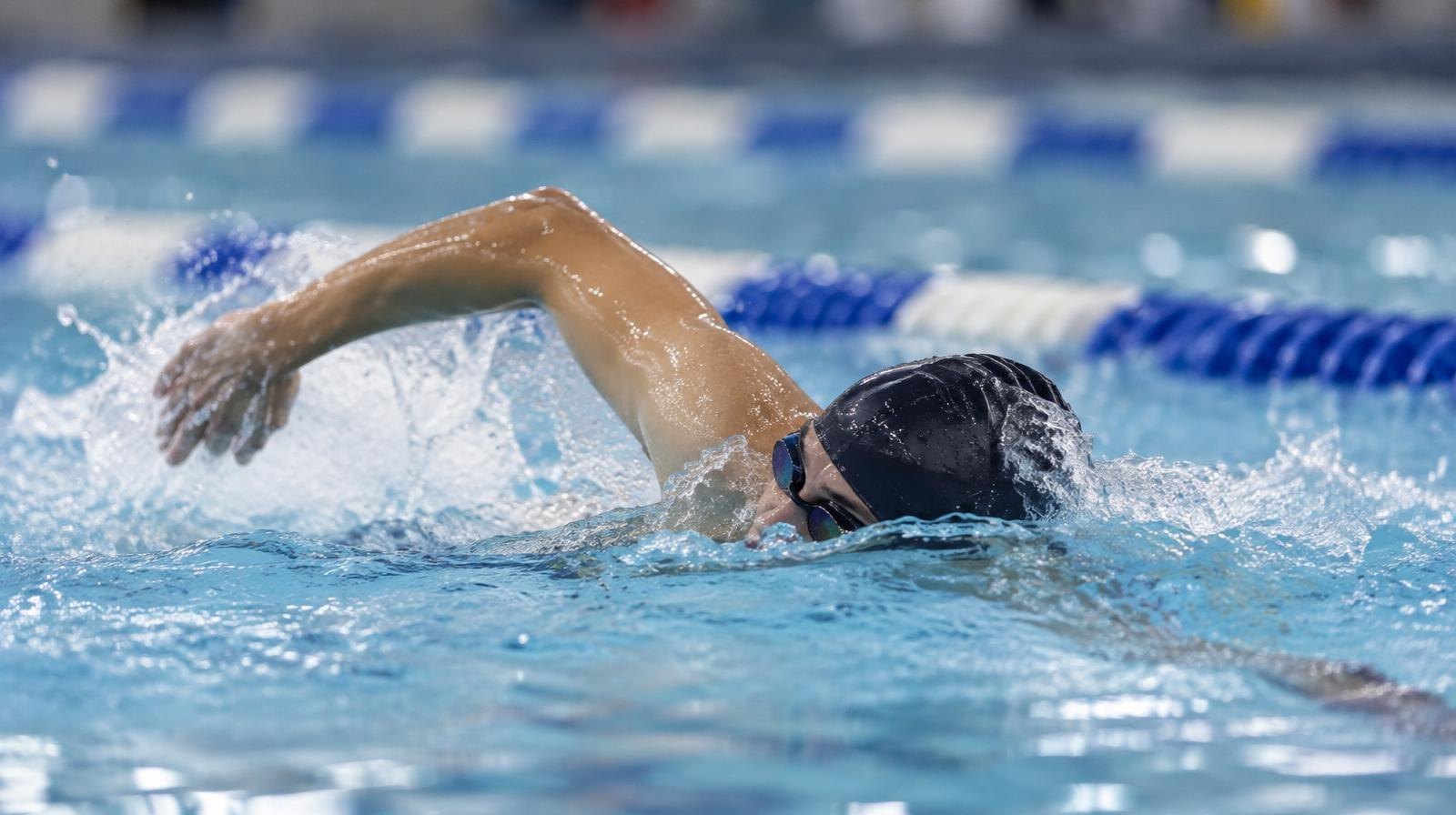 Swimmer mid-stroke in a competitive indoor pool lane with blue lane lines.