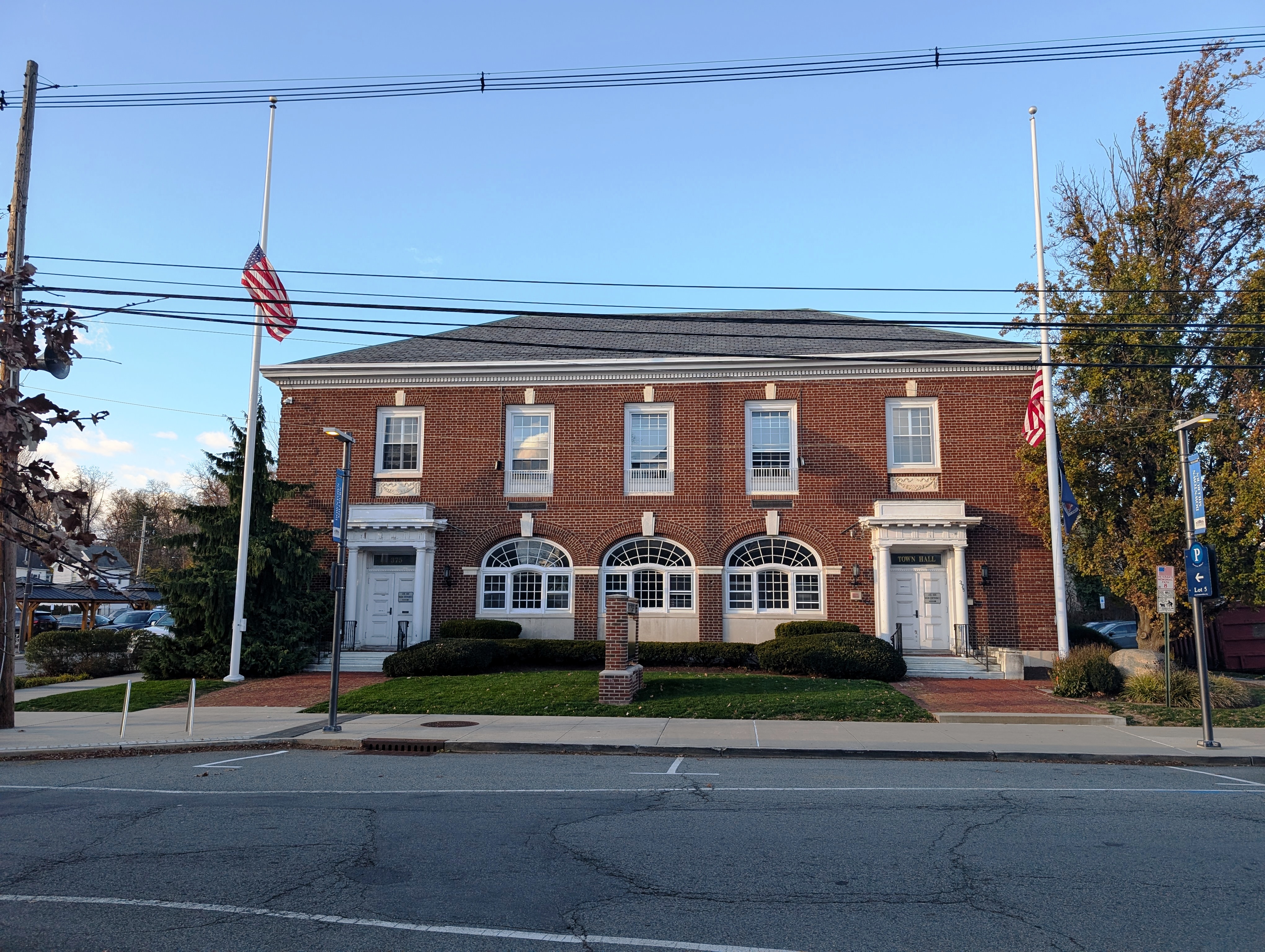 Two-story red brick municipal building with arched windows and American flags on flagpoles.