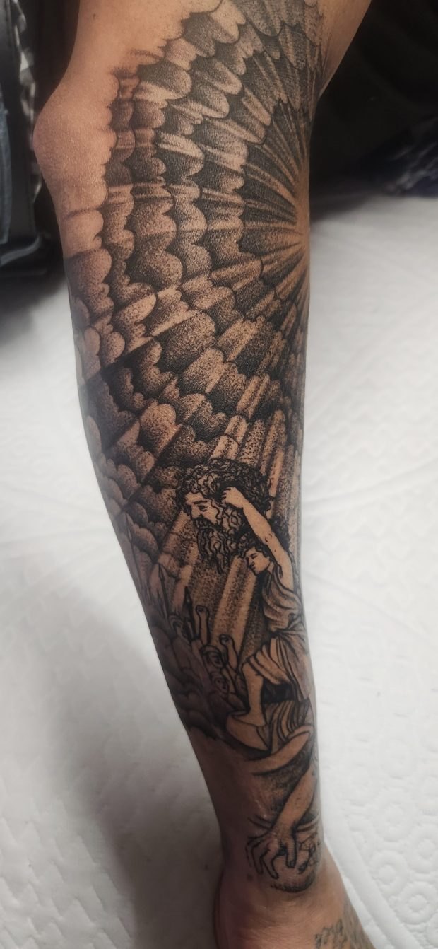 Close-up of a detailed black and gray tattoo depicting a large winged figure on a person's lower leg.