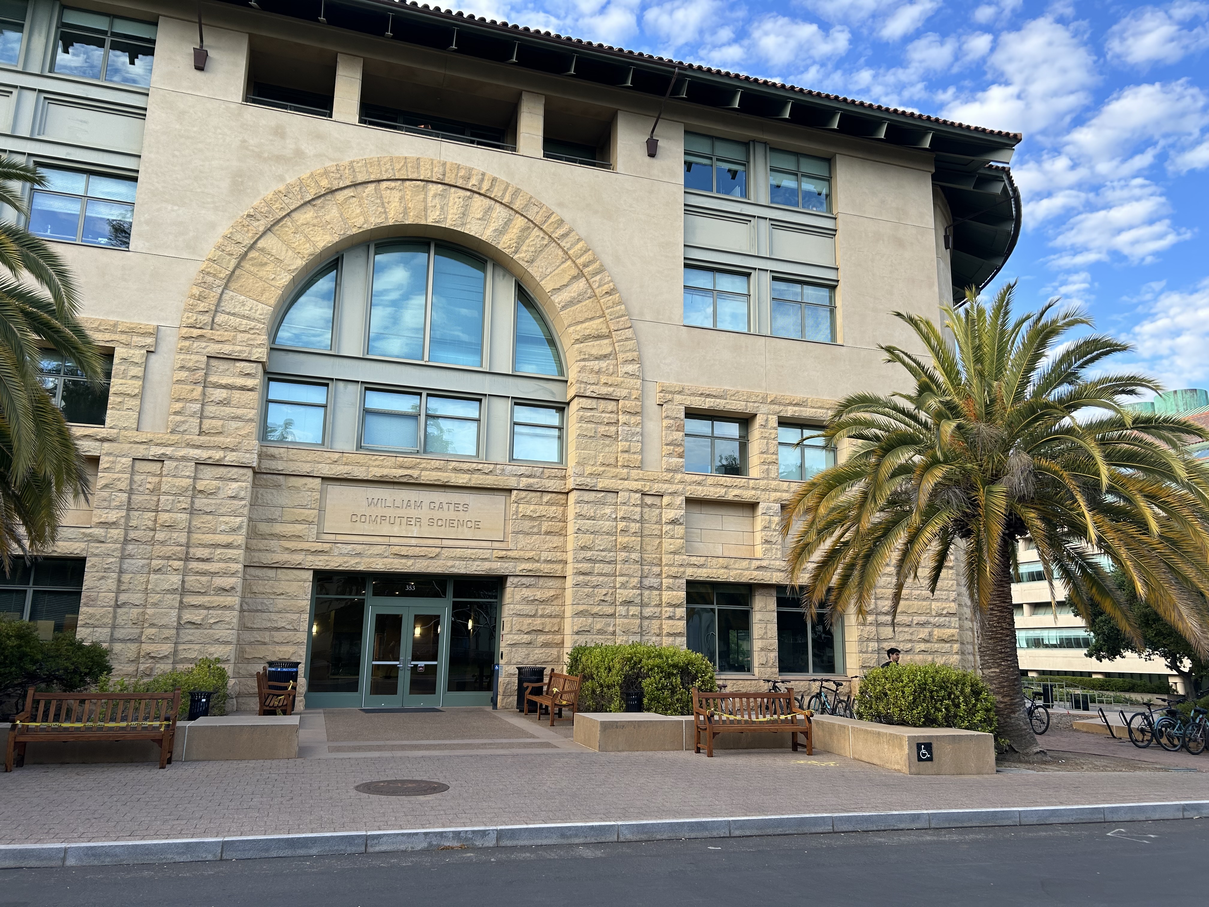 Stone building with arched entrance and palm trees, labeled William Gates Computer Science.