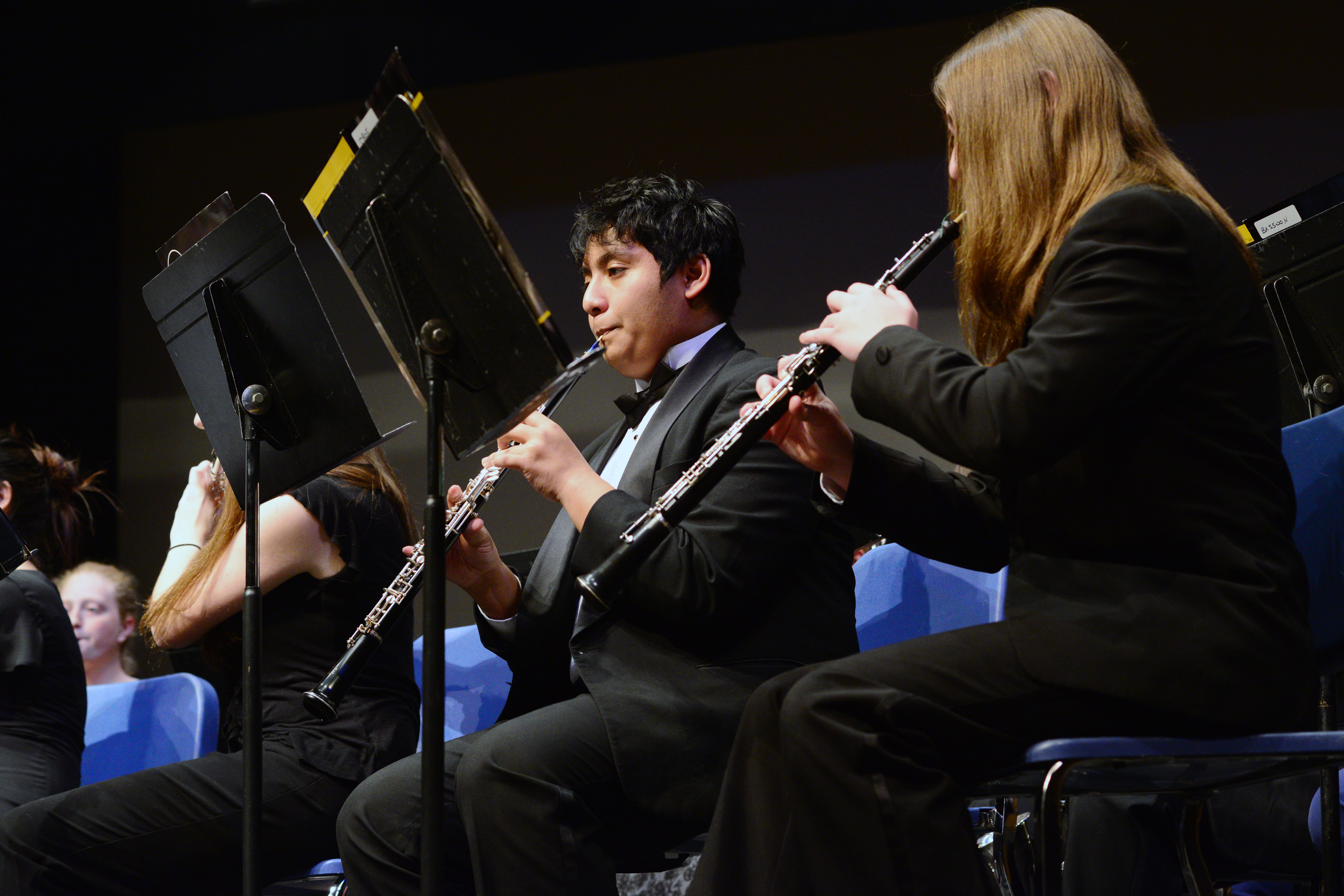 Two students in black formal attire play woodwind instruments at music stands.