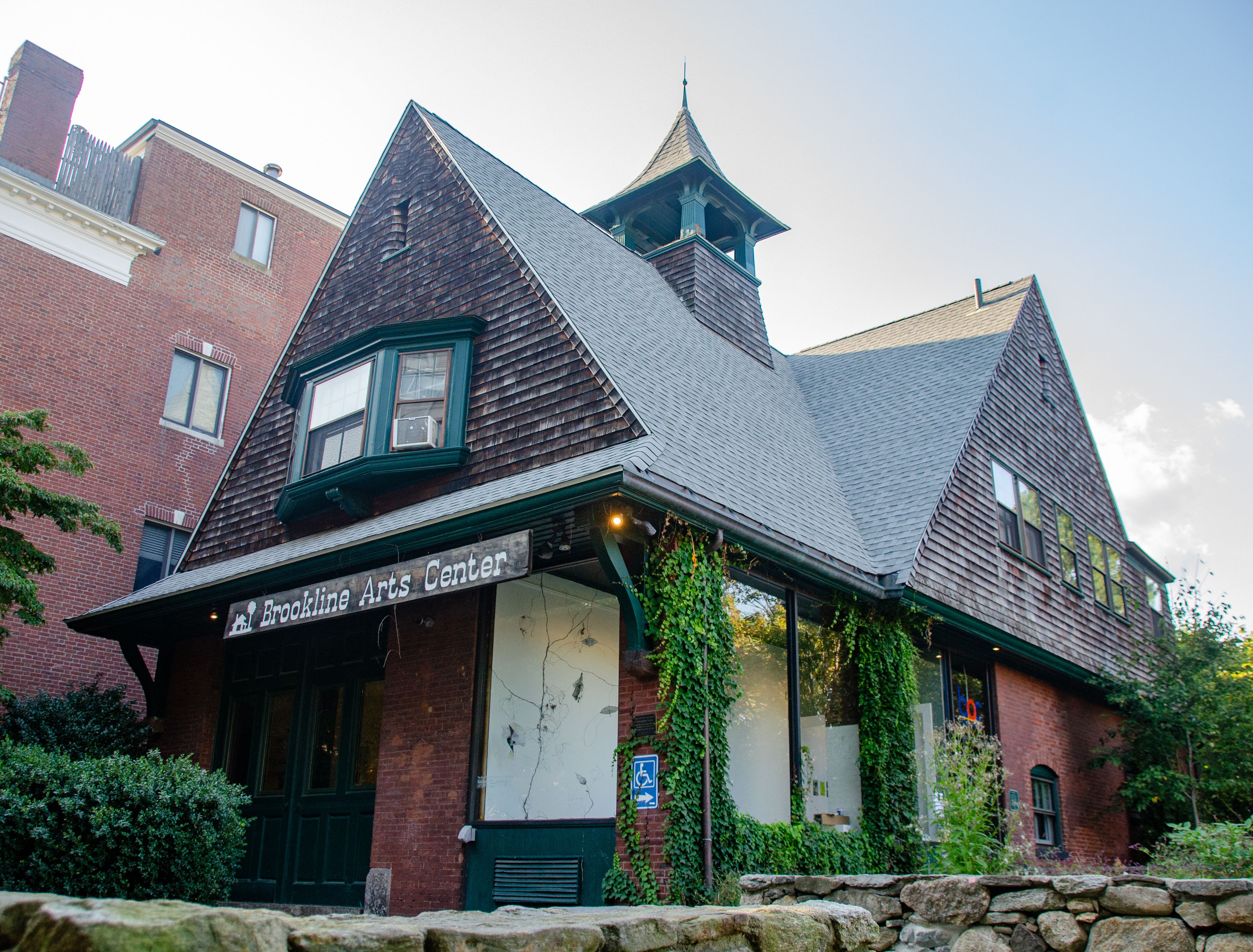 Ivy-covered historic firehouse building with steep gabled roofs and a Brookline Arts Center sign.