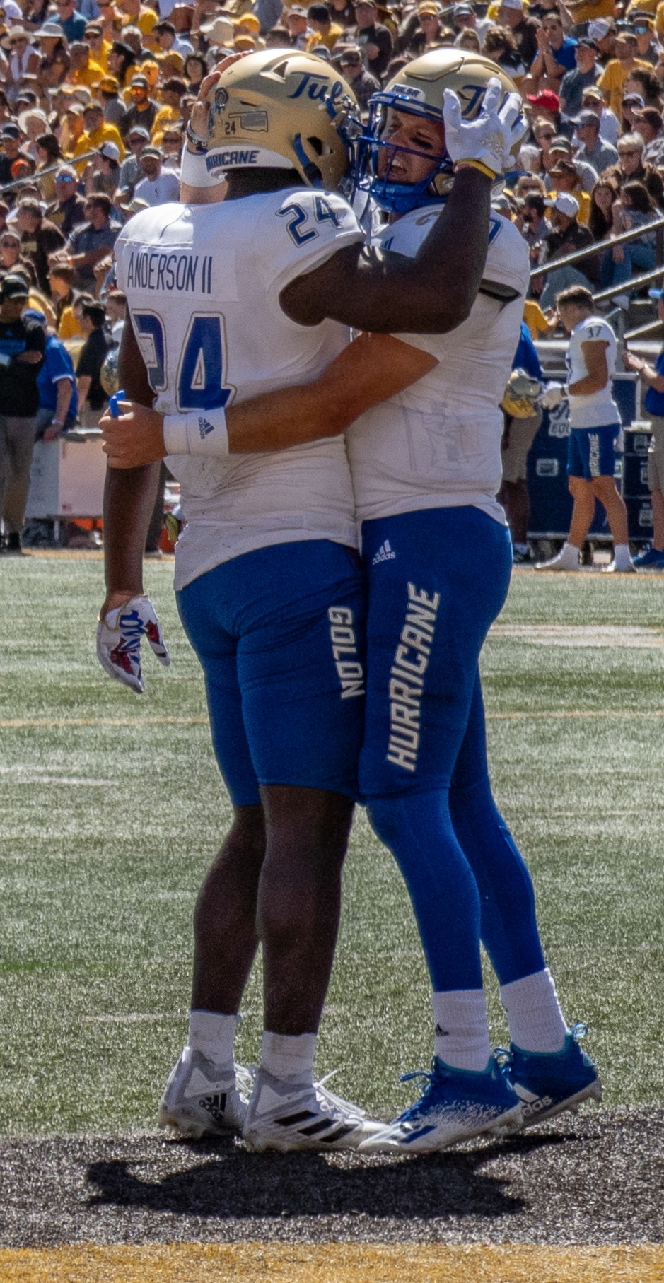 Two college football players in blue and gold uniforms embracing on the field.