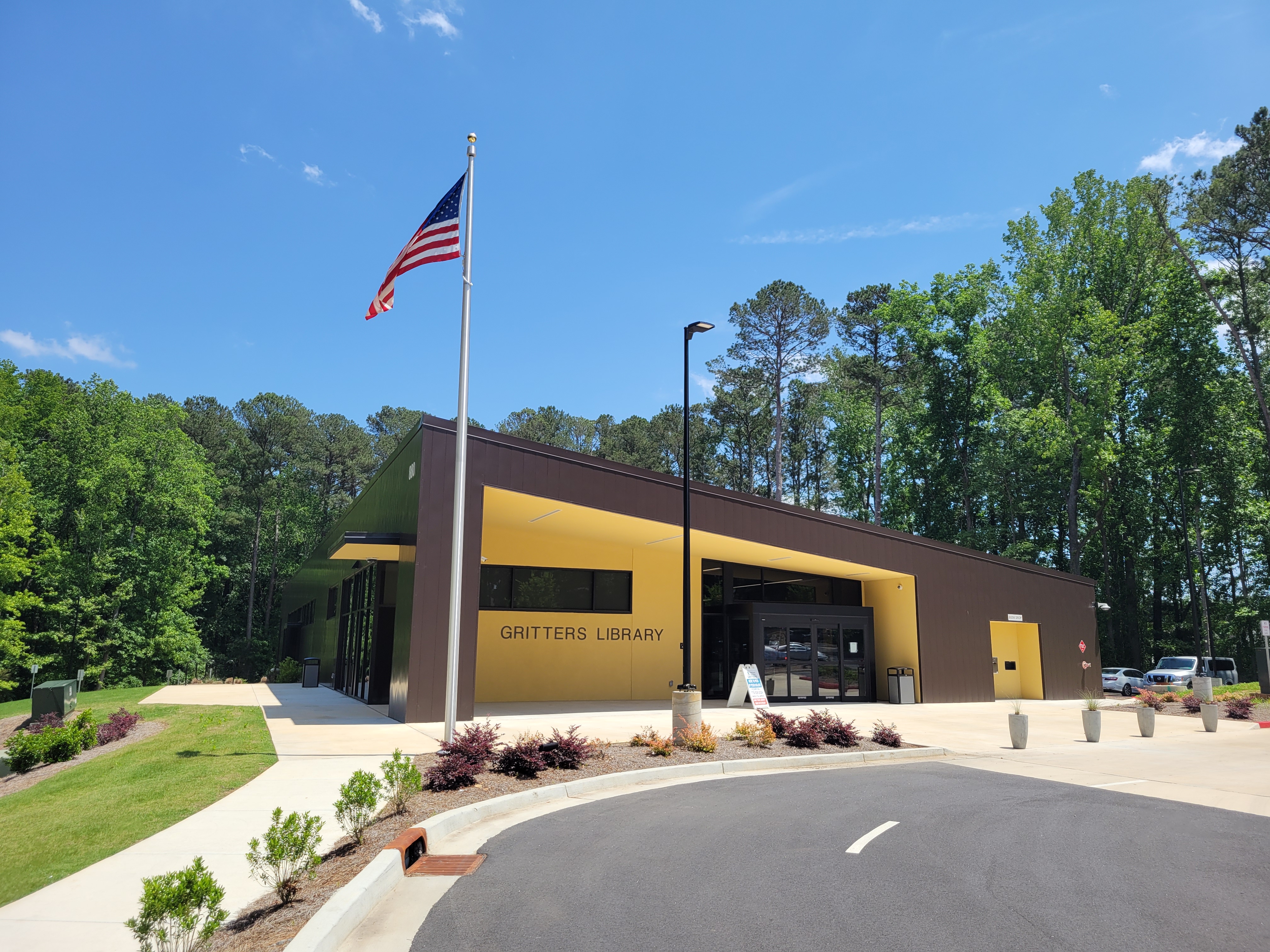 Exterior of a single-story library building with an American flag and parking lot.