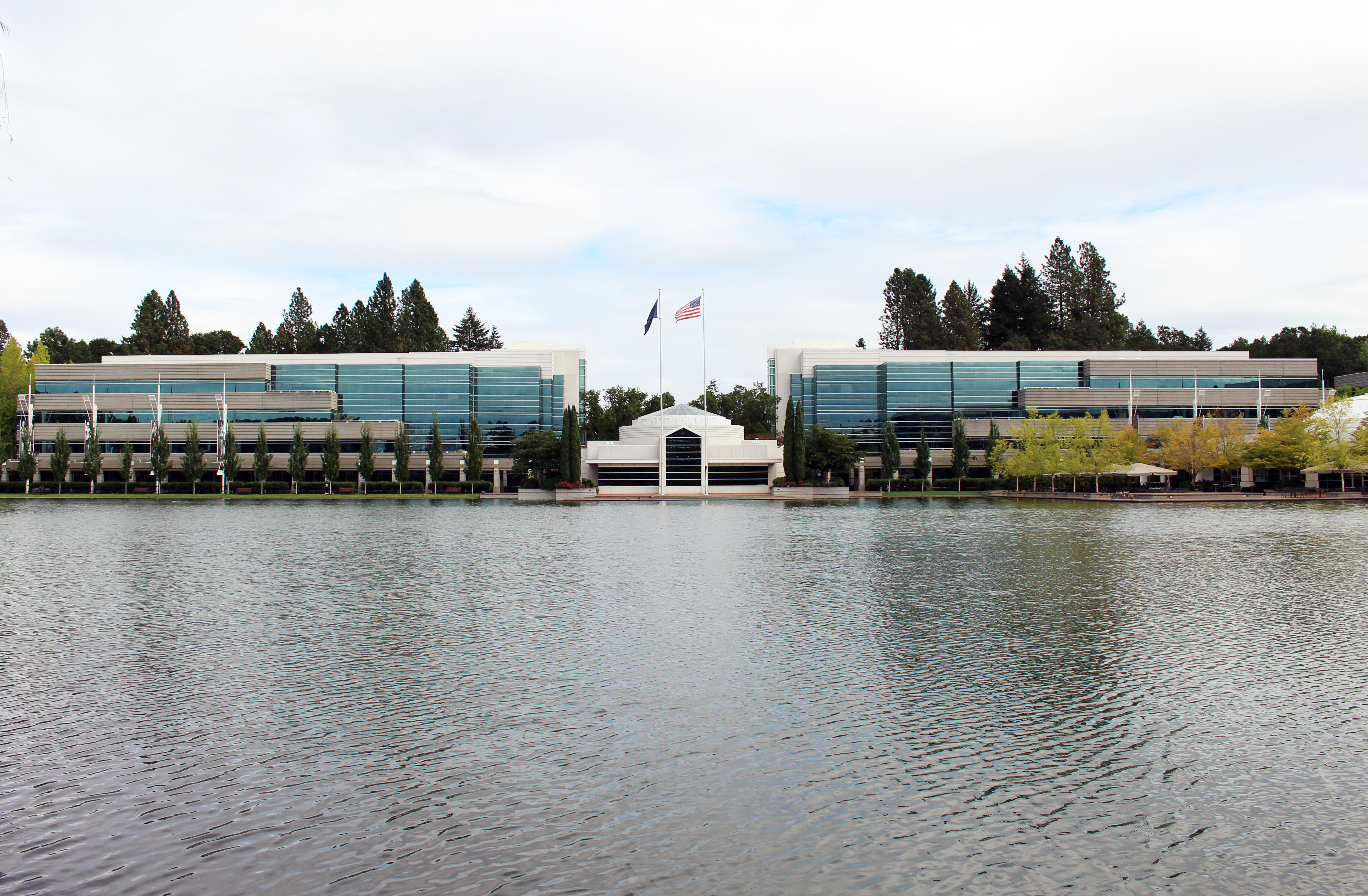 Two large glass office buildings flanking a walkway, reflected in a pond.
