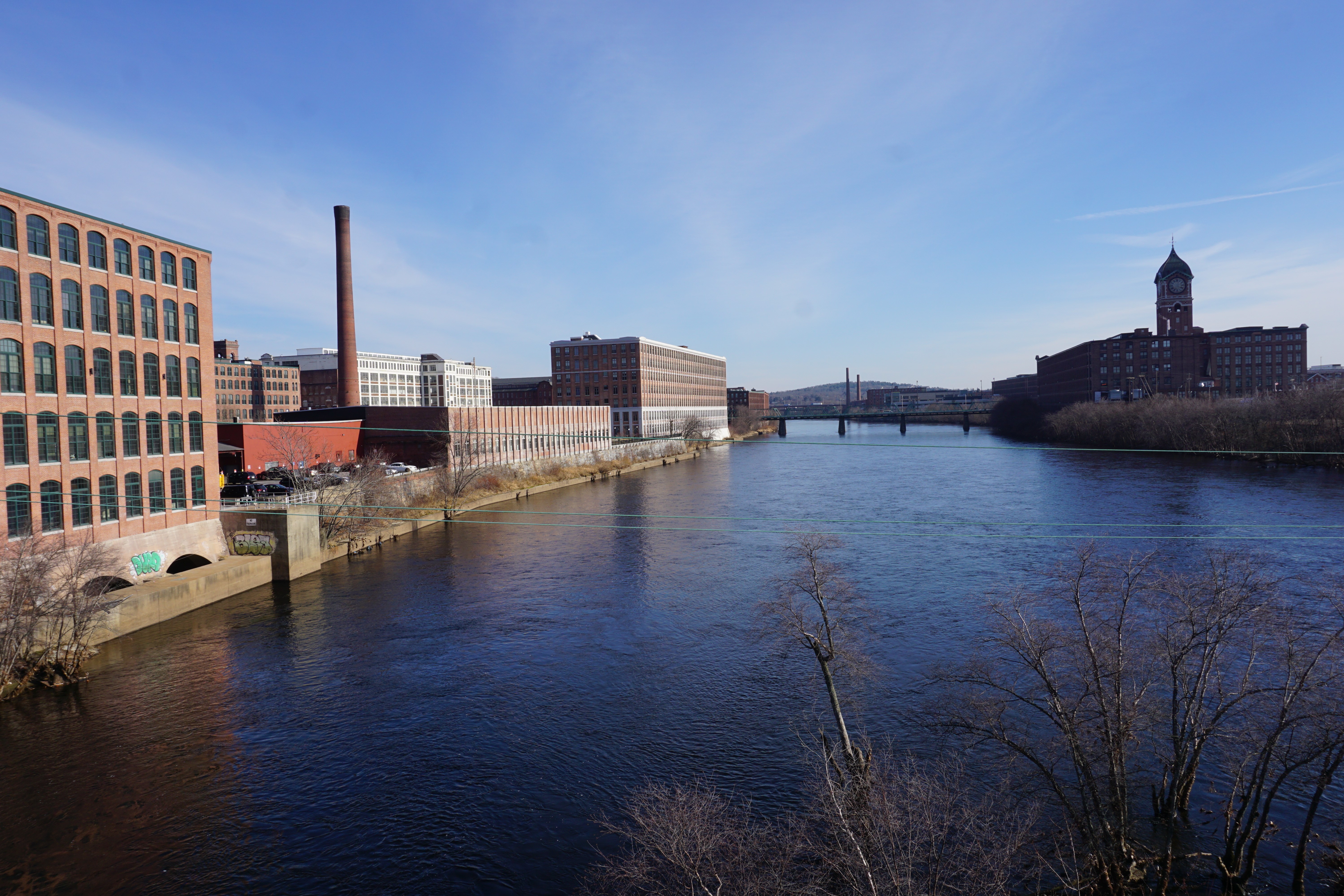 Wide river flanked by historic brick mill buildings under a clear winter sky.