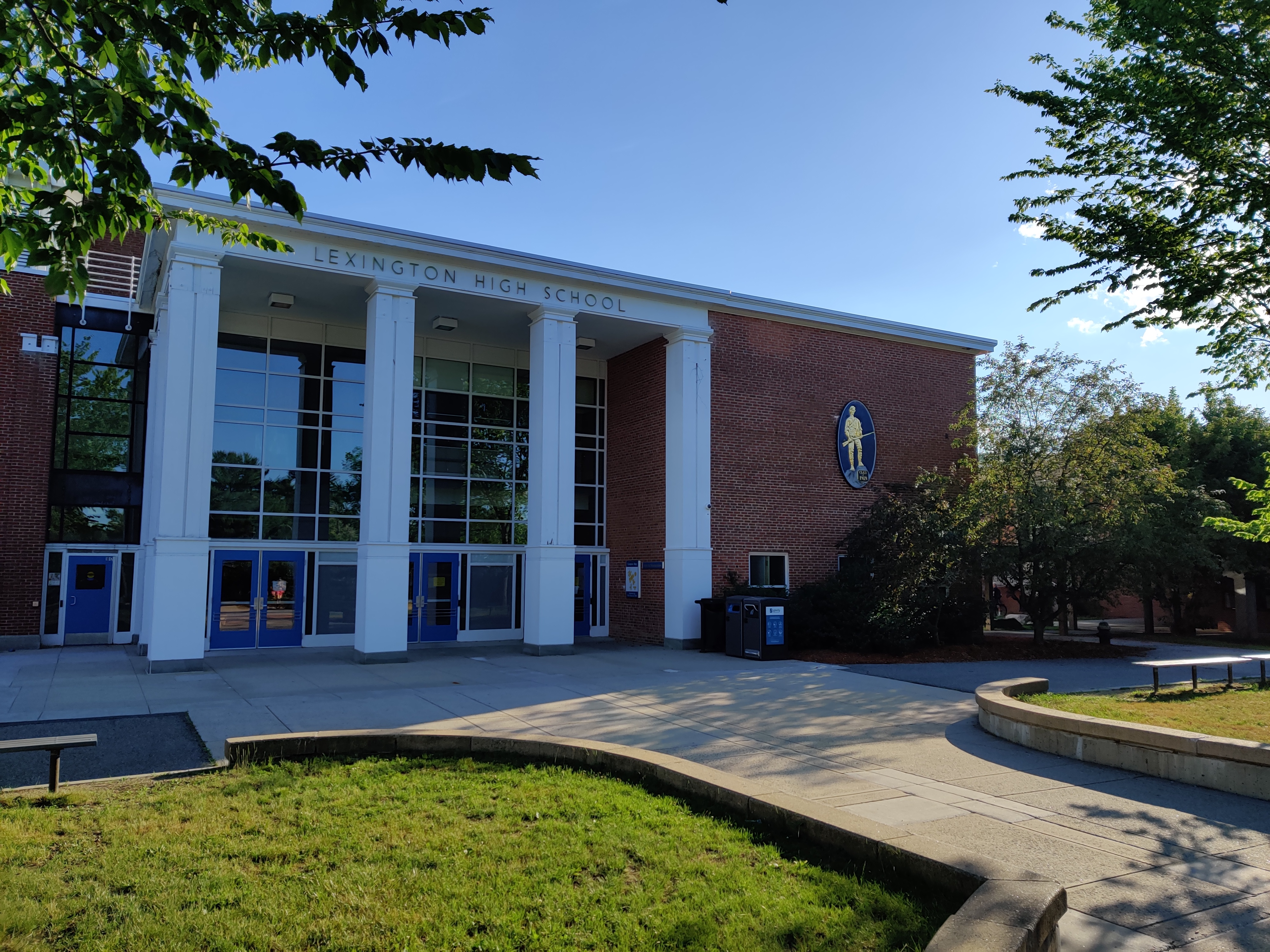 Brick school building with white columns and blue doors, viewed from a paved quad