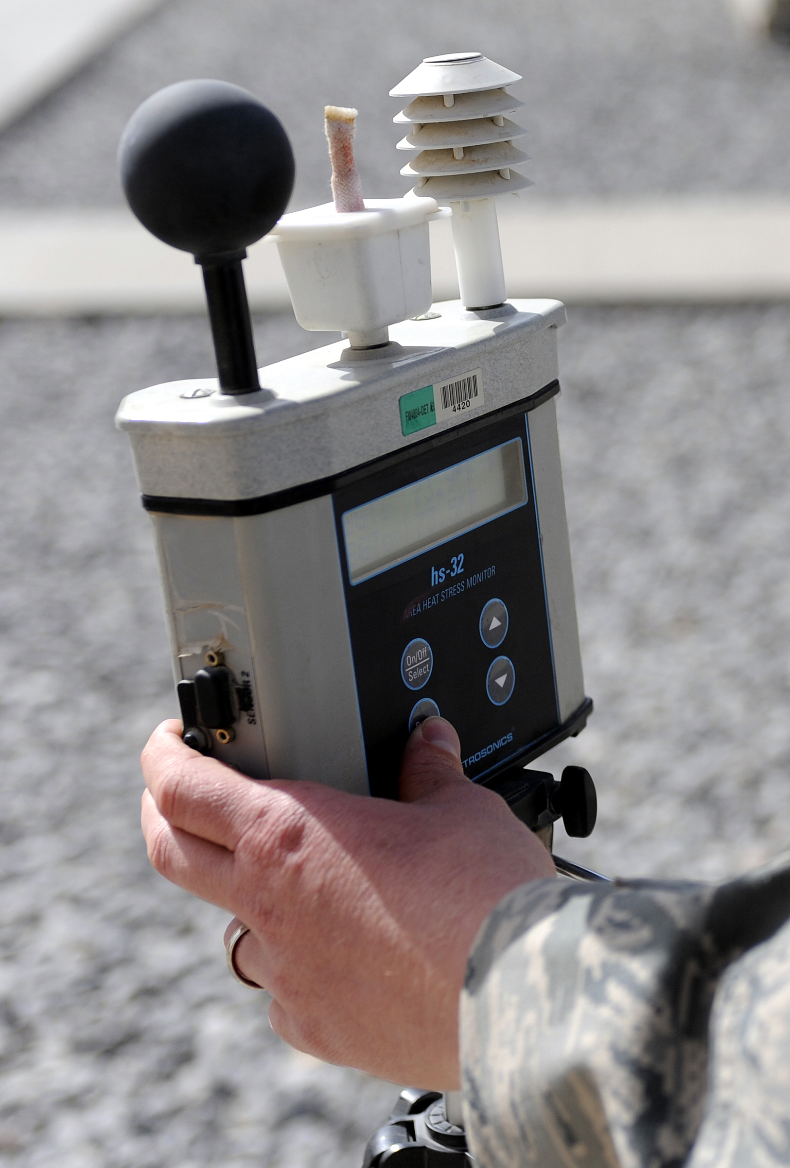 Person in military uniform holding a portable WBGT monitor with a black globe sensor.