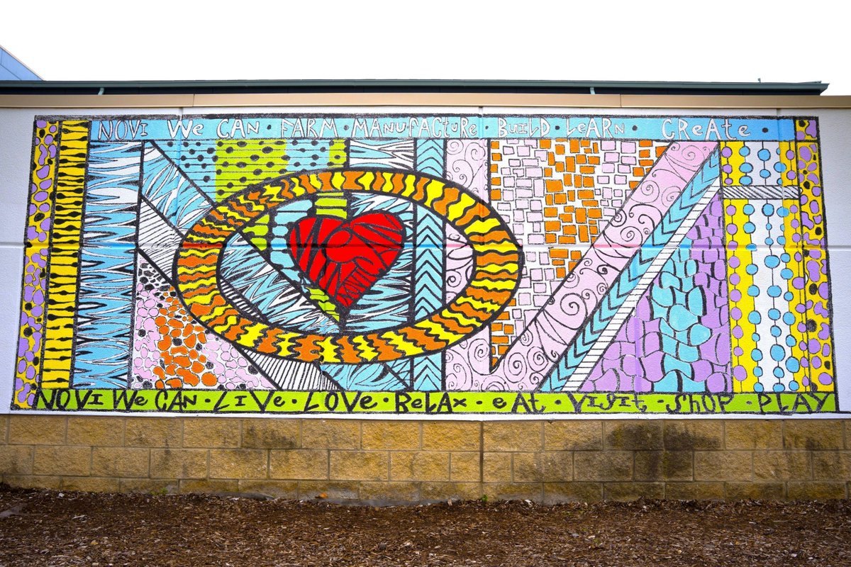 Colorful outdoor mural on a building wall with a red heart, geometric patterns, and hand-lettered text.