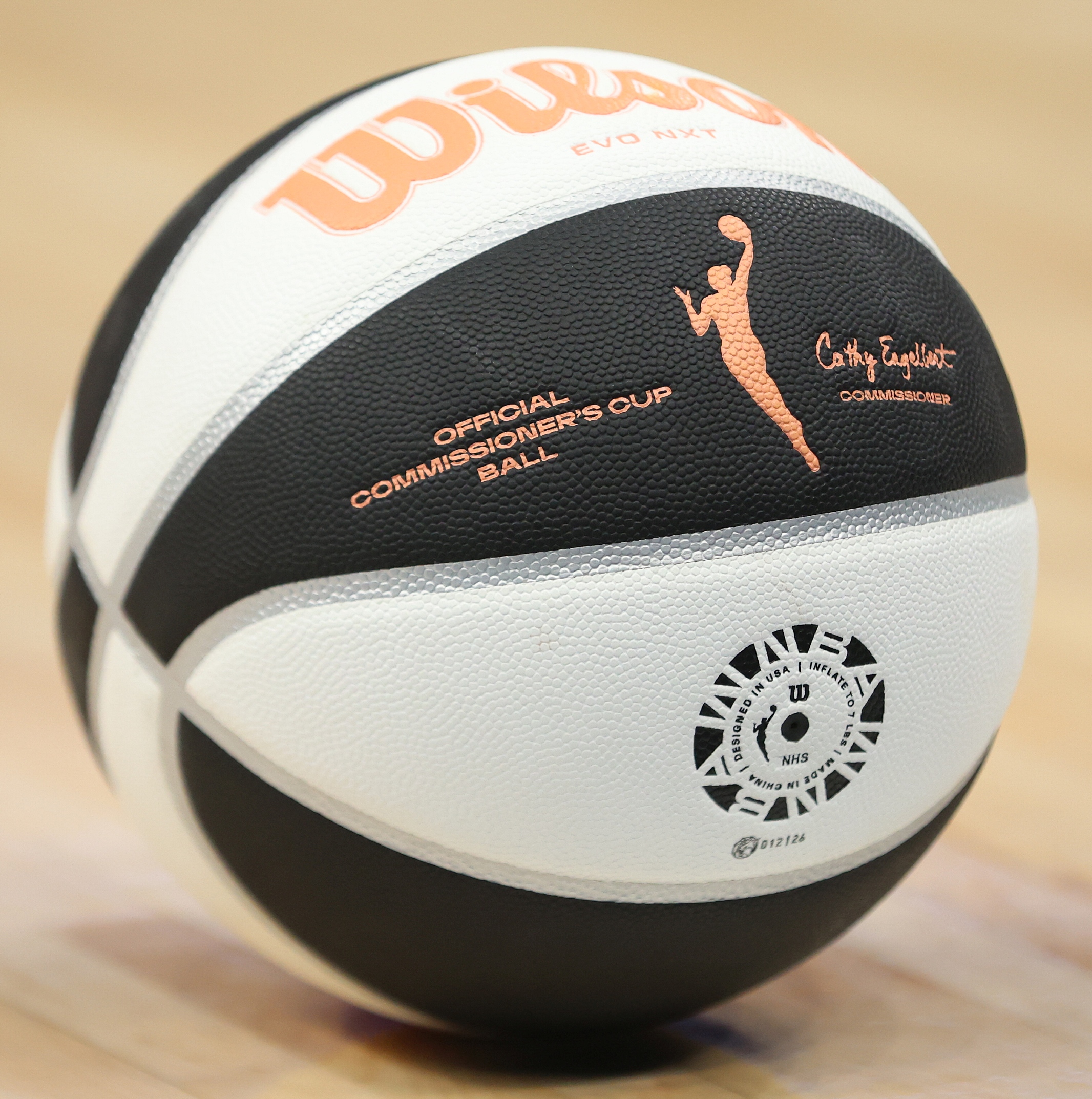Black and white WNBA Commissioner's Cup basketball resting on a hardwood court floor.